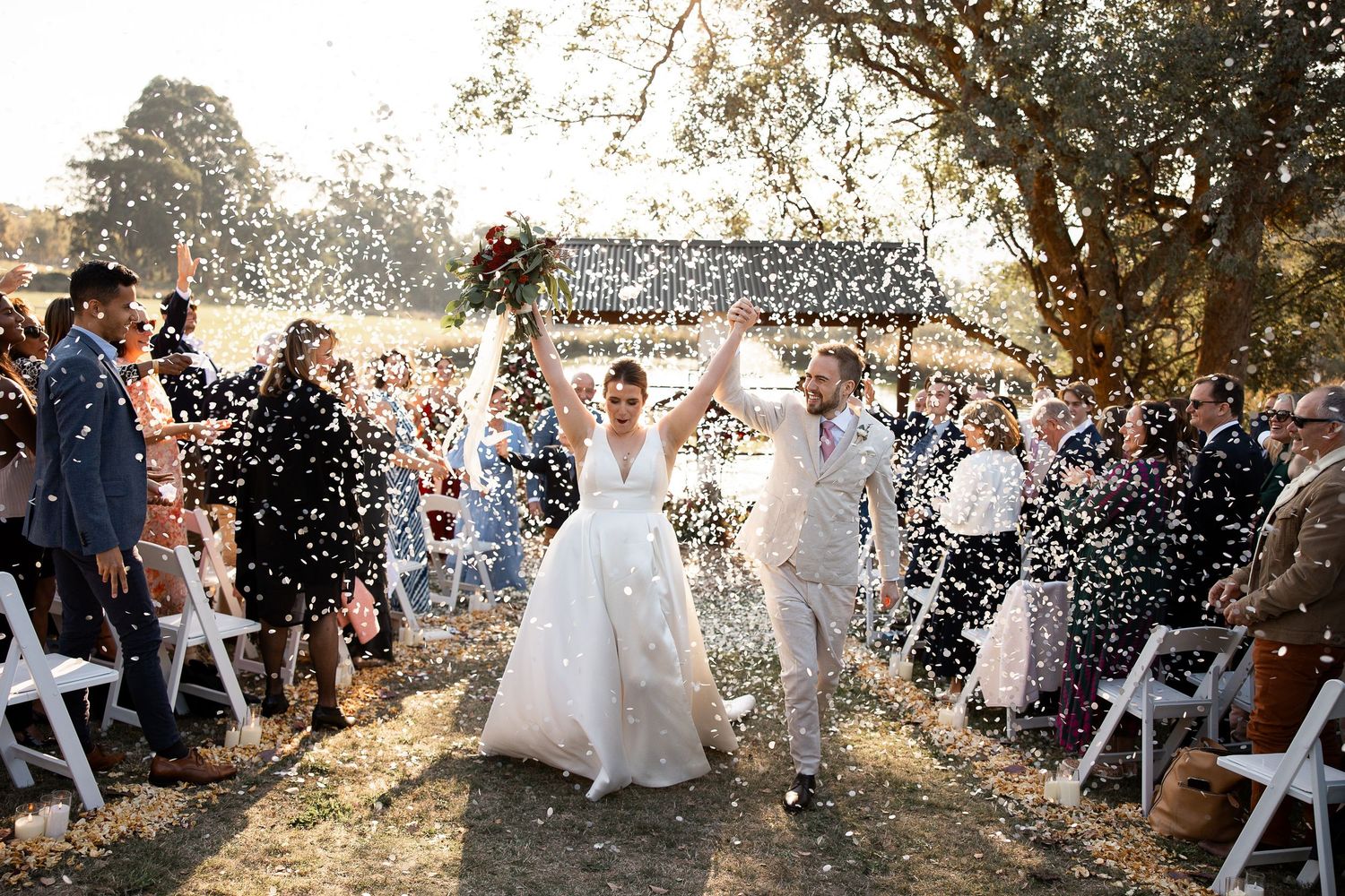 Wedding guests shower newlyweds with confetti during outdoor daytime celebration at sunny venue.
