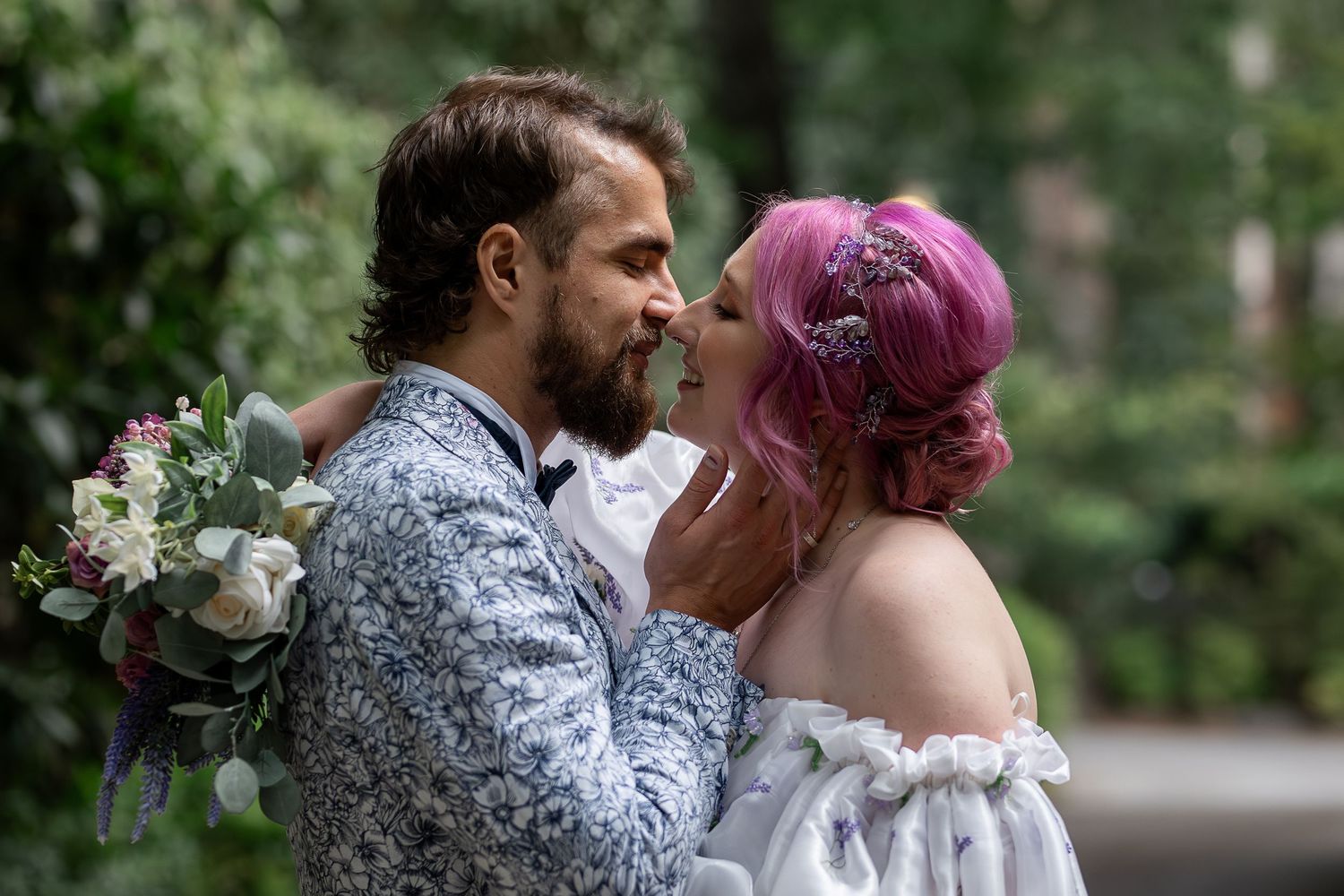 A couple shares an intimate moment at their wedding, with the bride wearing white and sporting vibrant pink hair.