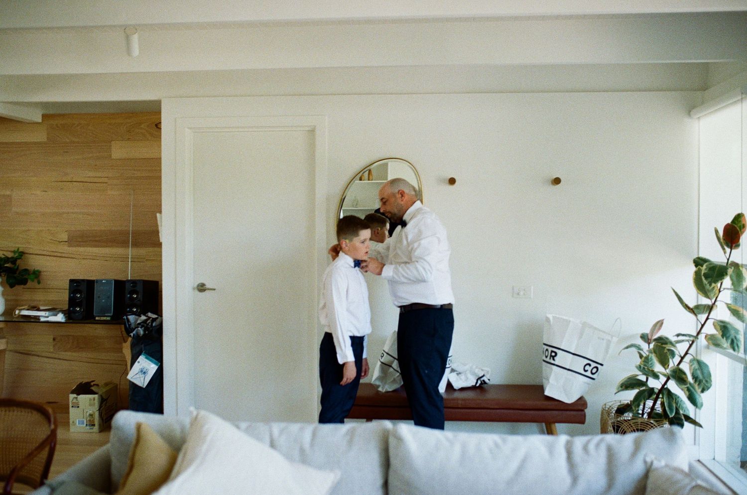 Grandfather helping grandson with tie in modern living room, family bonding moment at home.