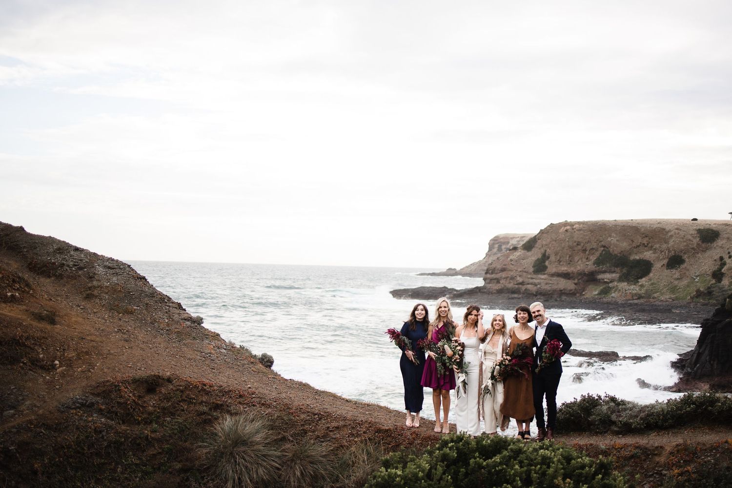 Small group stands on rugged coastal cliffs overlooking dramatic ocean views during a misty day.