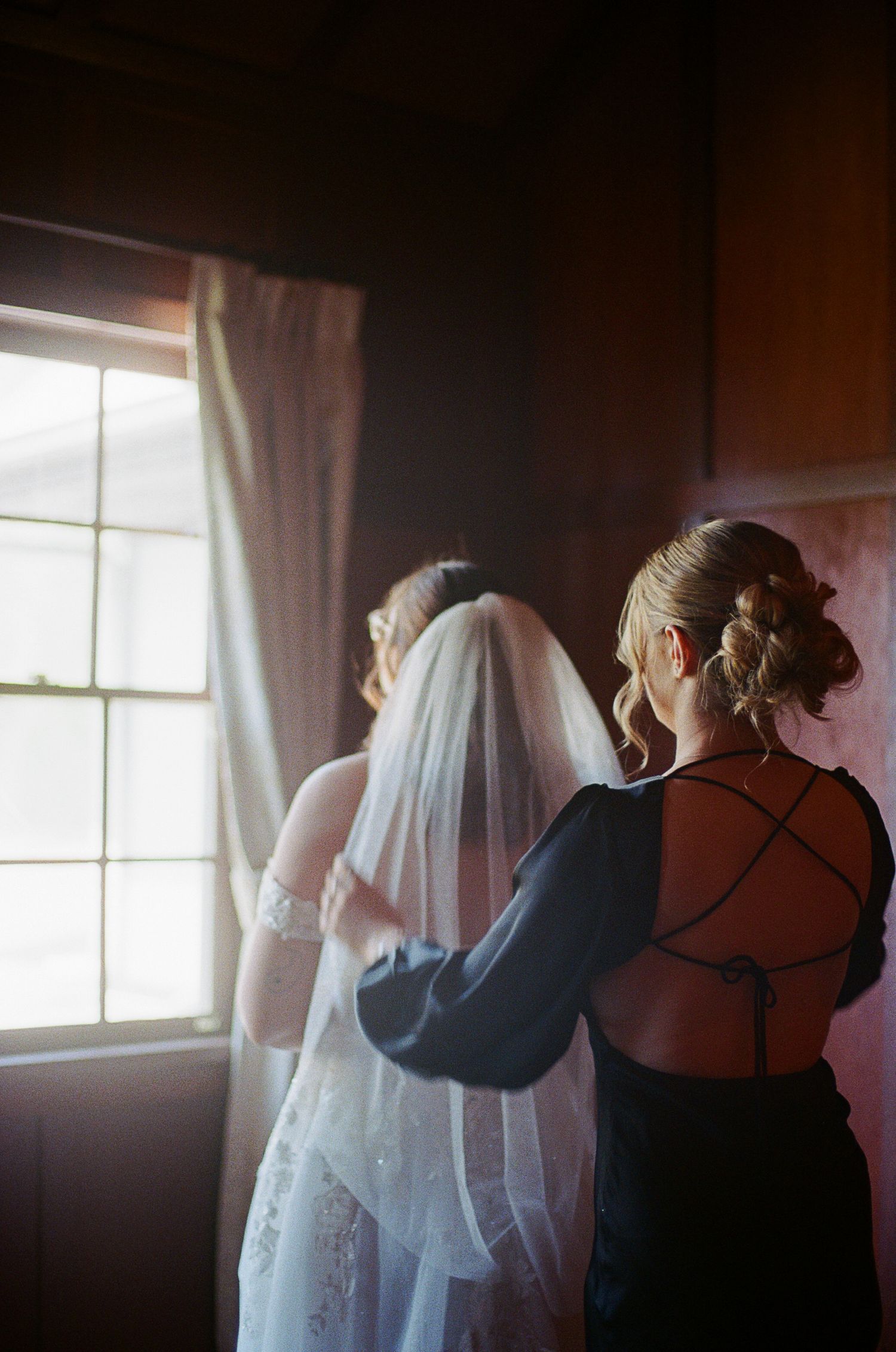 Two people stand silhouetted against a window with curtains in a moody indoor scene.