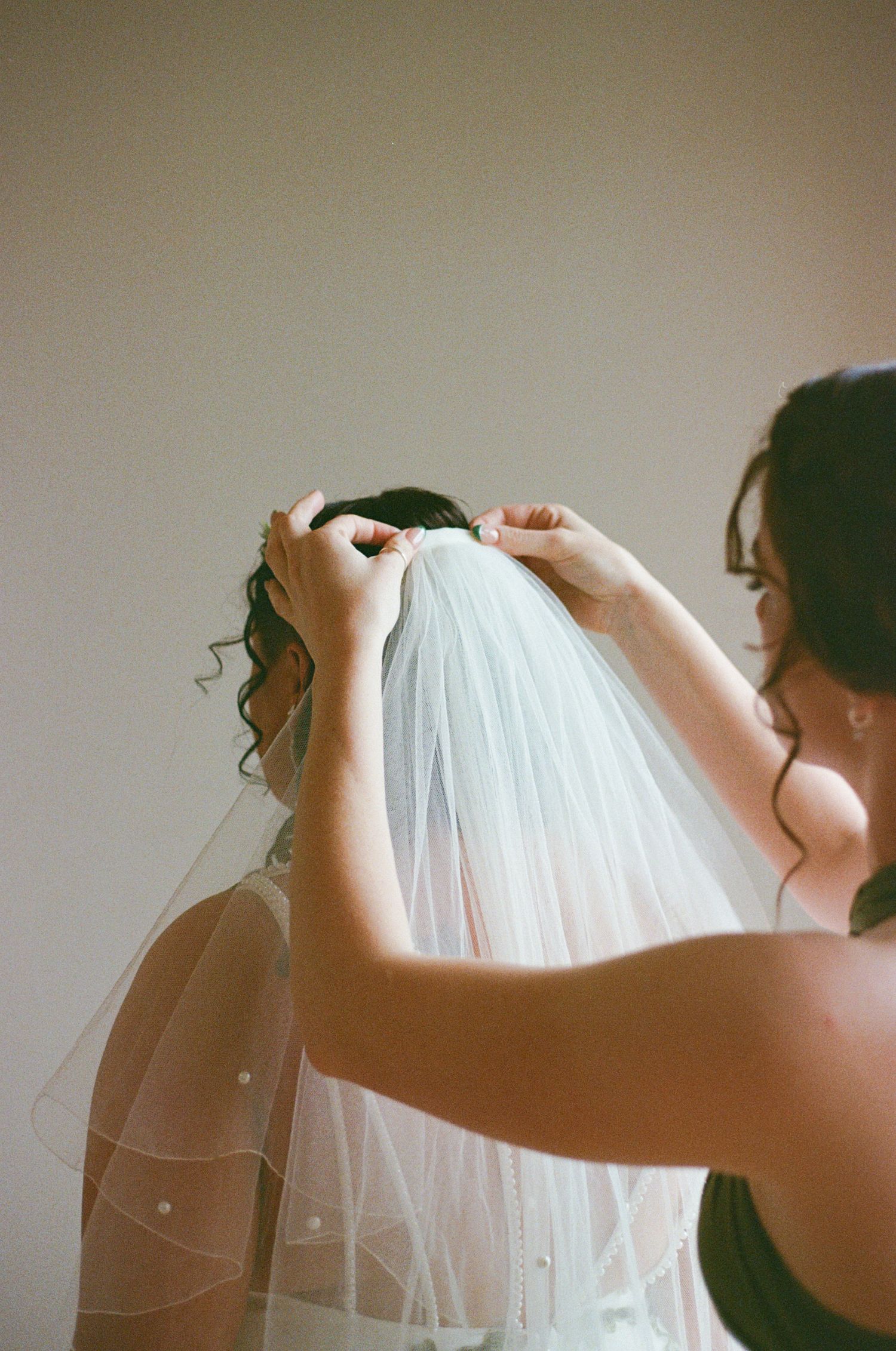 A bridesmaid carefully pins a wedding veil into the bride's updo hairstyle before the ceremony.