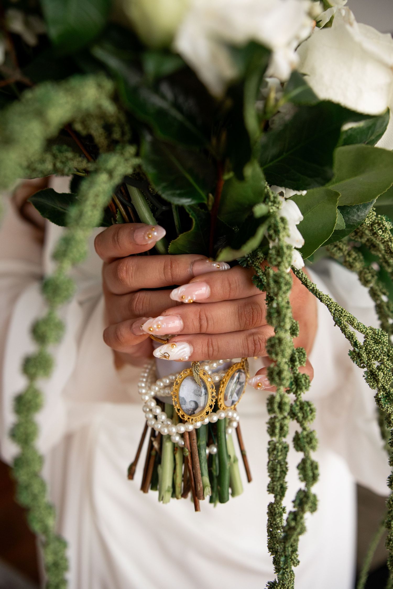 Bride holding white floral bouquet with pearl jewelry wrap, featuring elegant nail art with gold details.