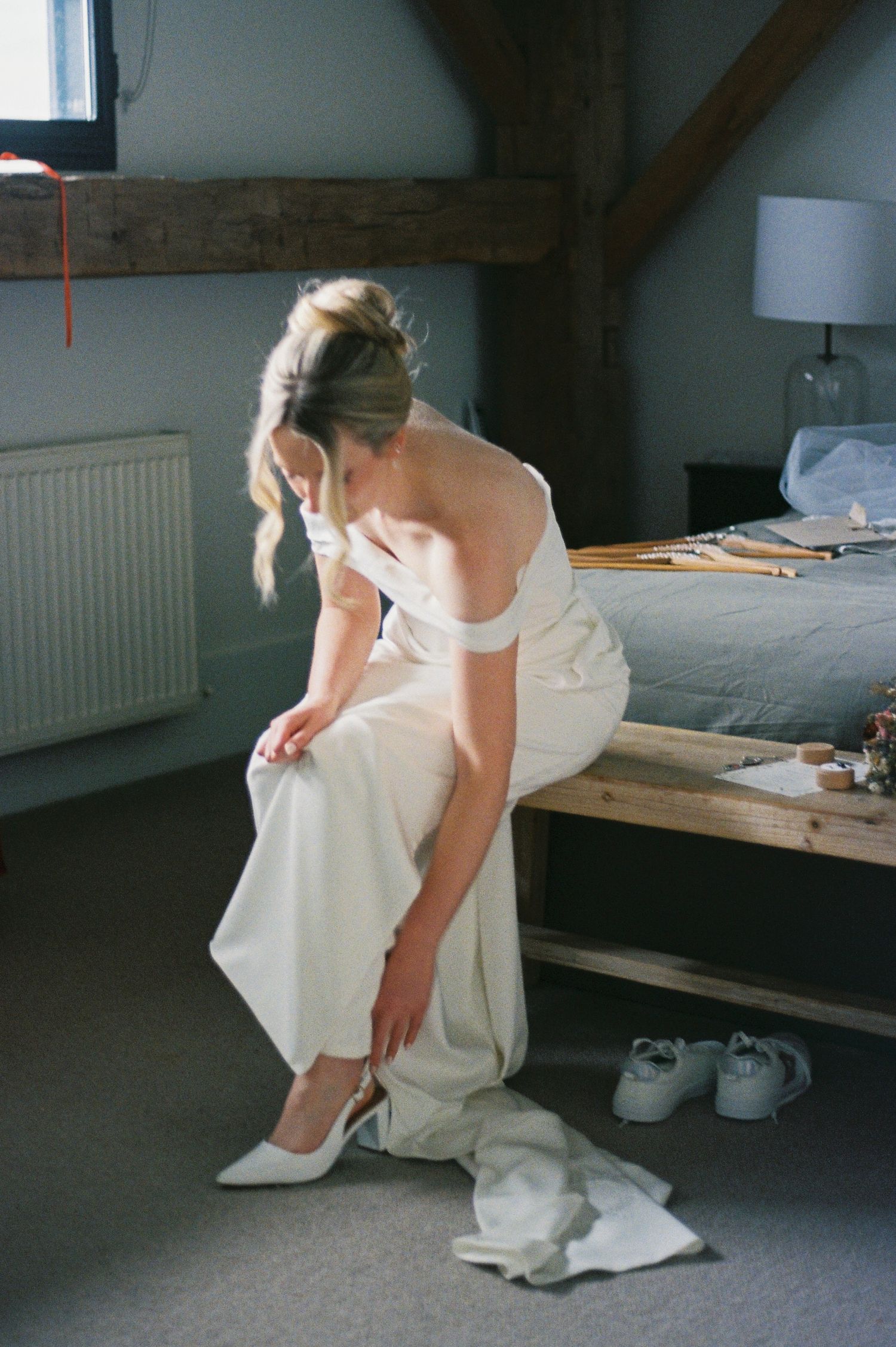 A figure in white clothing sits on a dark floor in a dimly lit room with minimal furnishings.