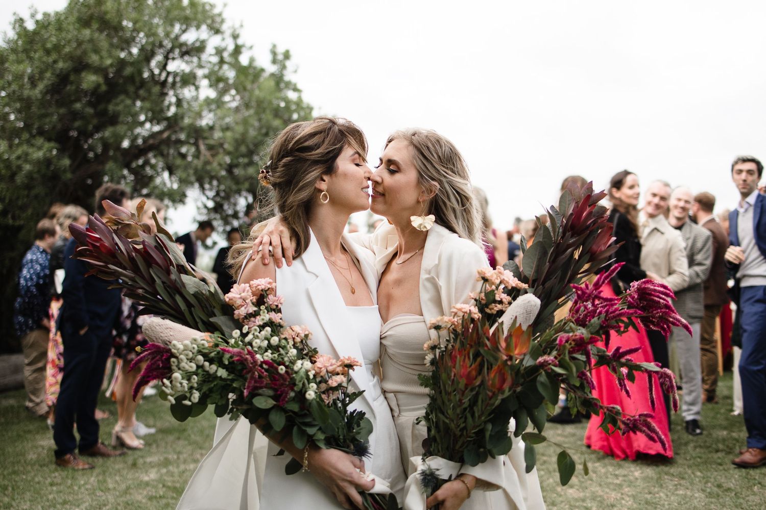 A joyful wedding celebration outdoors with large floral bouquets featuring burgundy and green blooms.