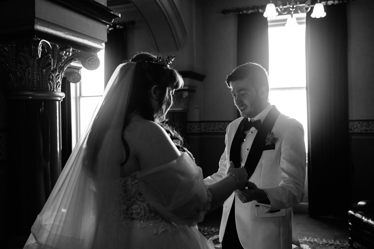 A tender black and white moment between a bride and groom bathed in window light during an intimate wedding ceremony.