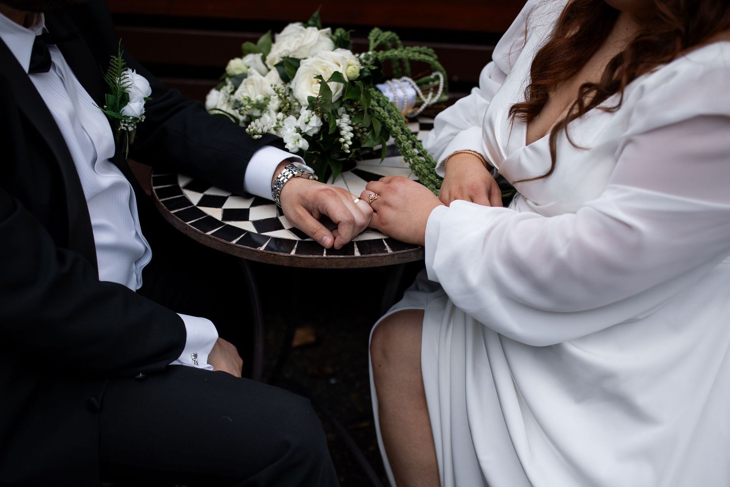 Bride and groom exchanging rings at wedding ceremony, with white floral bouquet on checkered table.