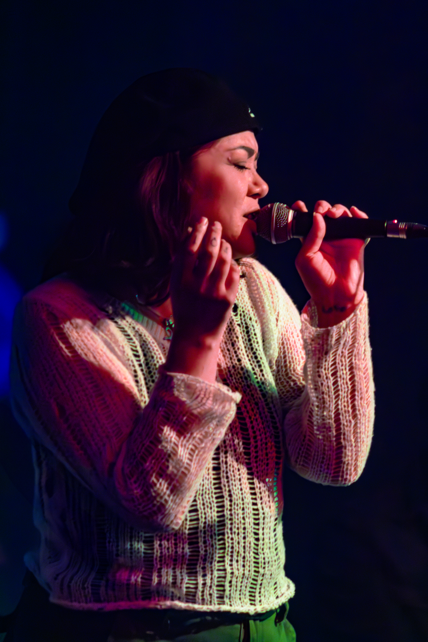 Singer performing on stage in knit sweater with dramatic purple and blue lighting at River North Icehouse in San Antonio, Texas.