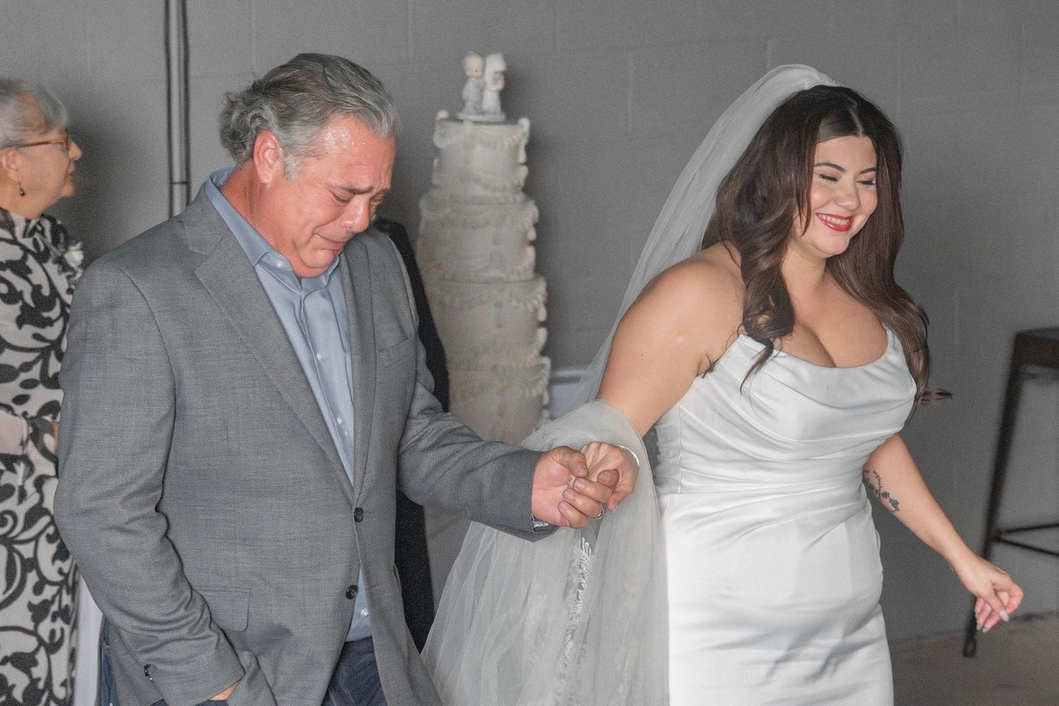 A bride in white dress walks hand in hand with someone in a grey suit.