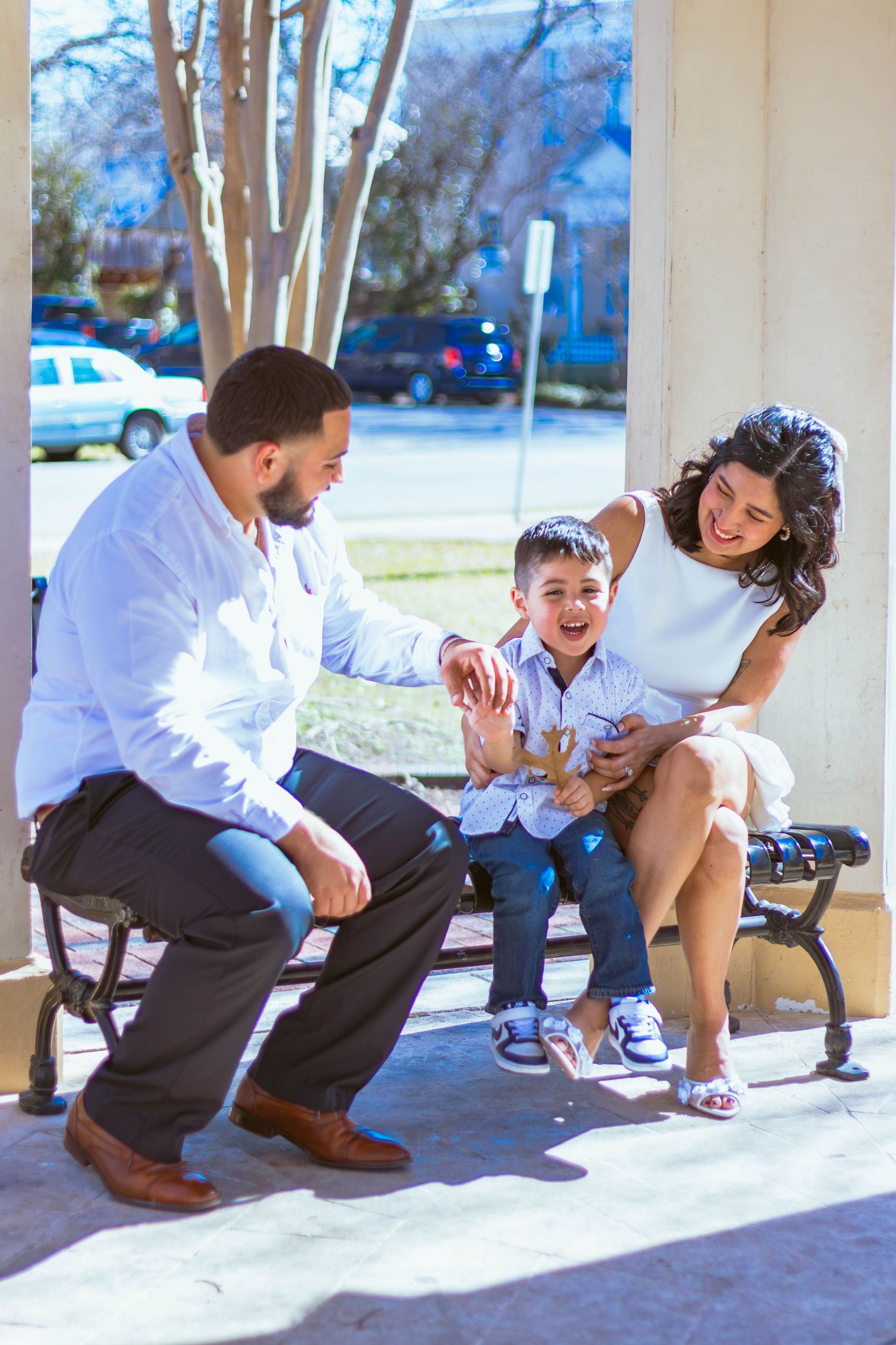 Family sharing a playful moment while sitting on a bench outside on a sunny day.