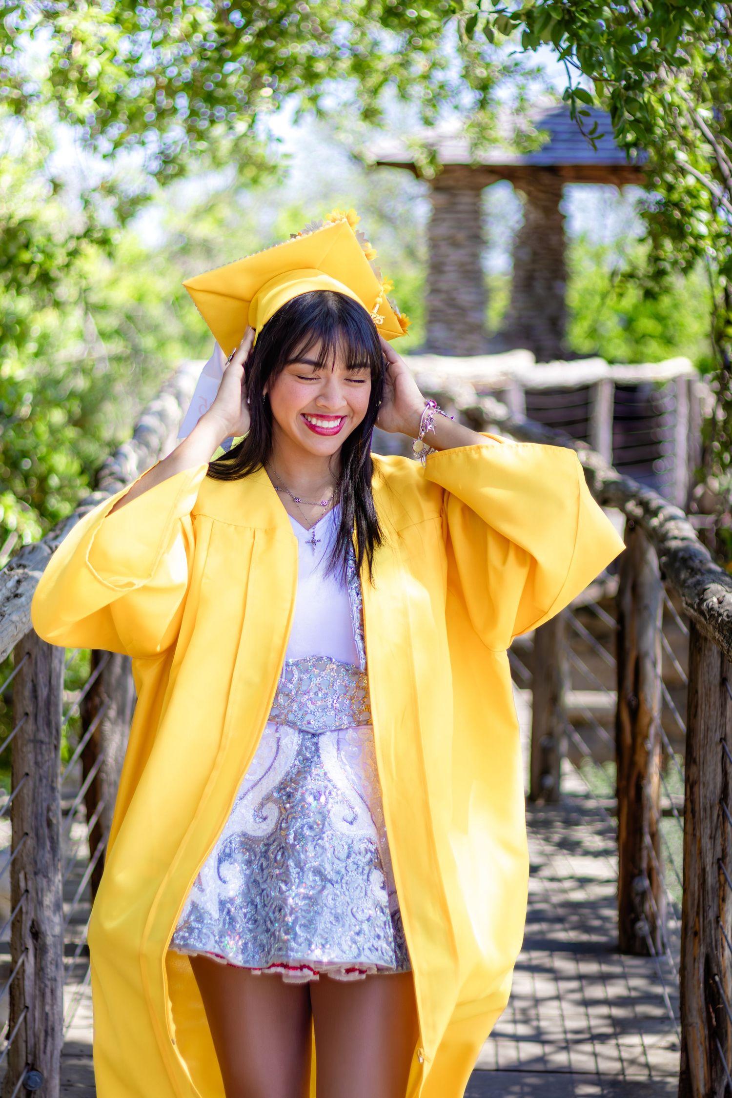 Graduate wearing bright yellow gown and cap smiles joyfully in outdoor garden setting.