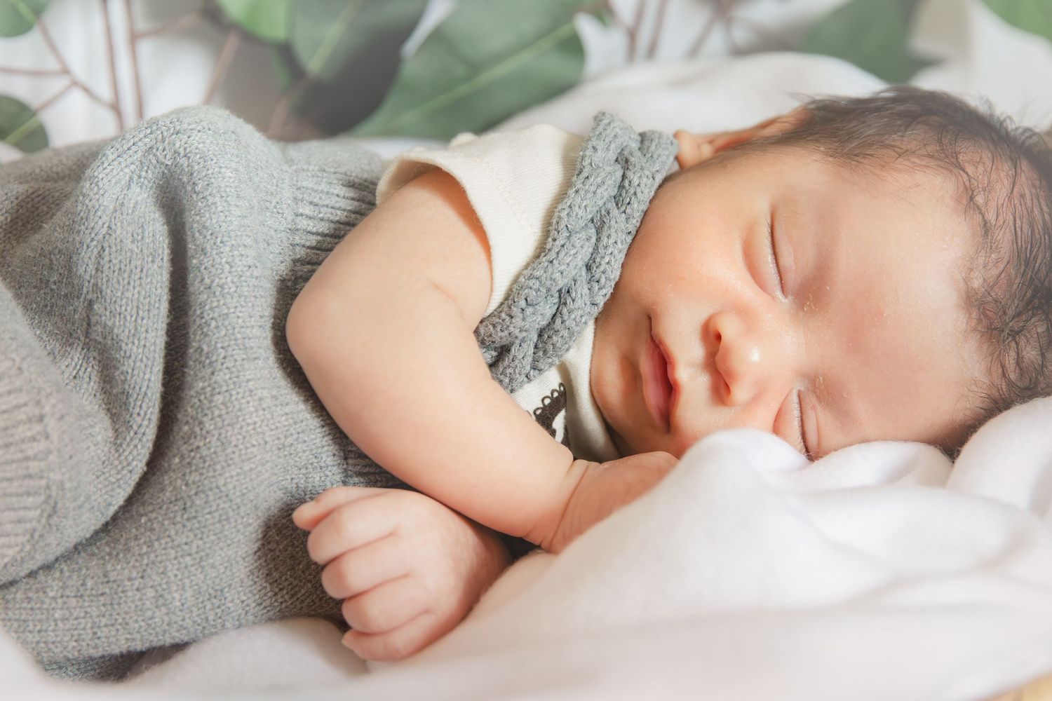 Peaceful sleeping baby wrapped in soft gray knit blanket resting on white bedding.