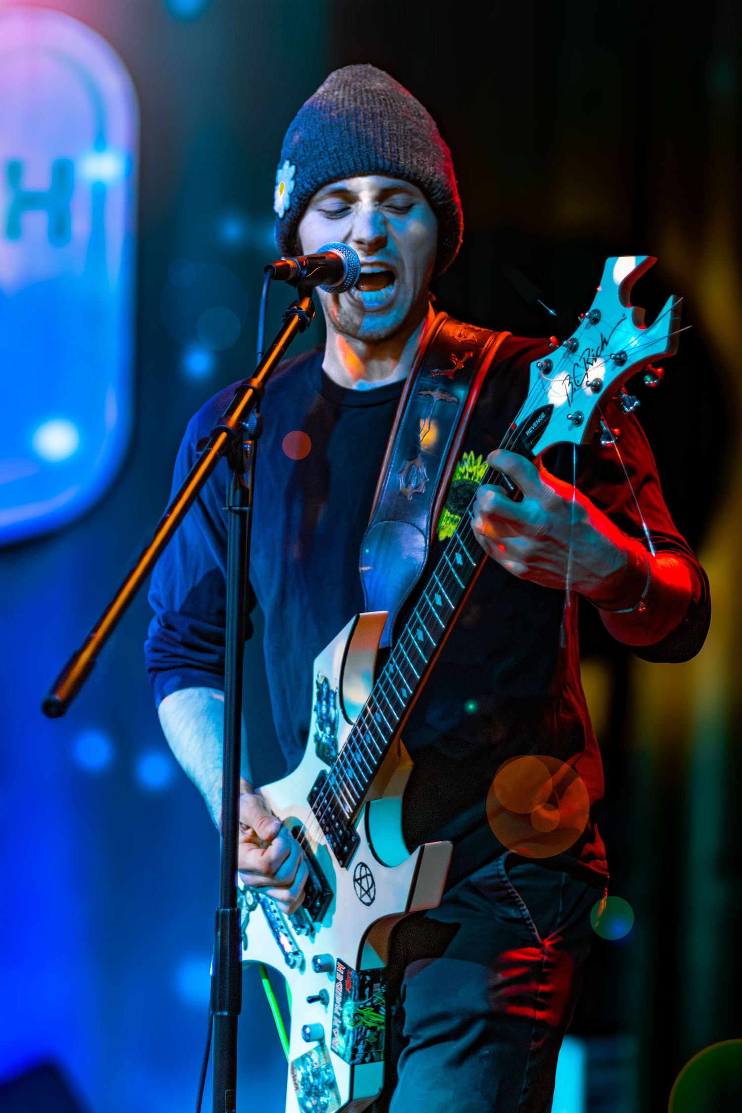Musician performs on stage with electric guitar under blue lighting.