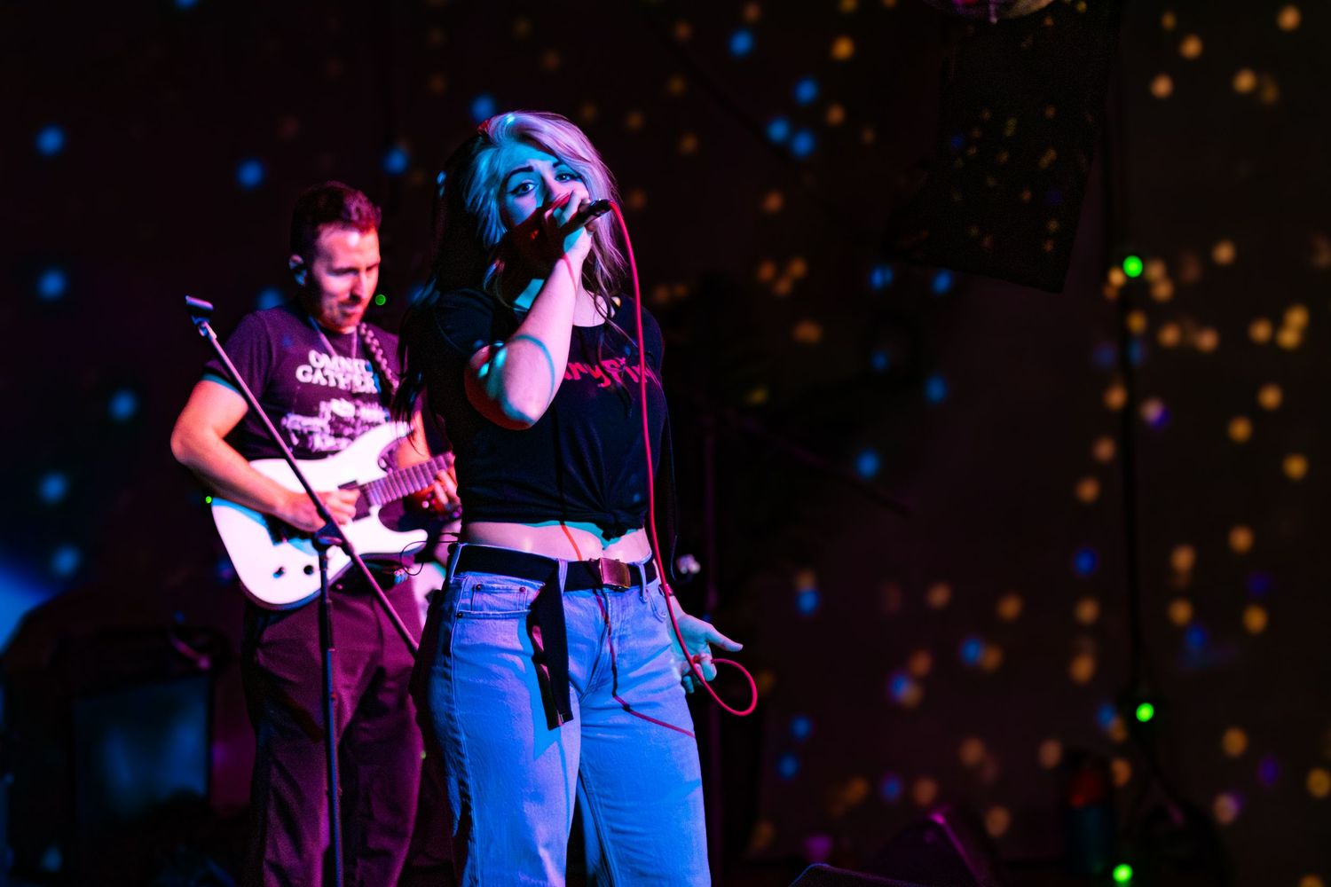 Musicians performing on stage with colorful spotlights and sparkly backdrop.