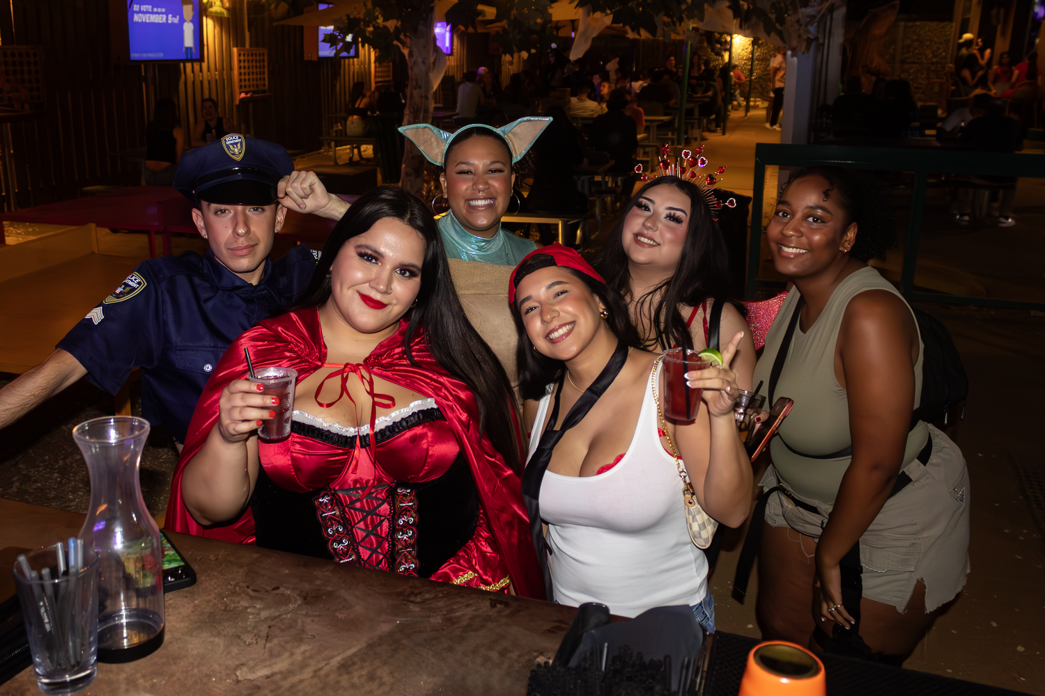 Group of friends posing with drinks at a nighttime social gathering for Halloween at Camp 1604 in San Antonio, Texas.