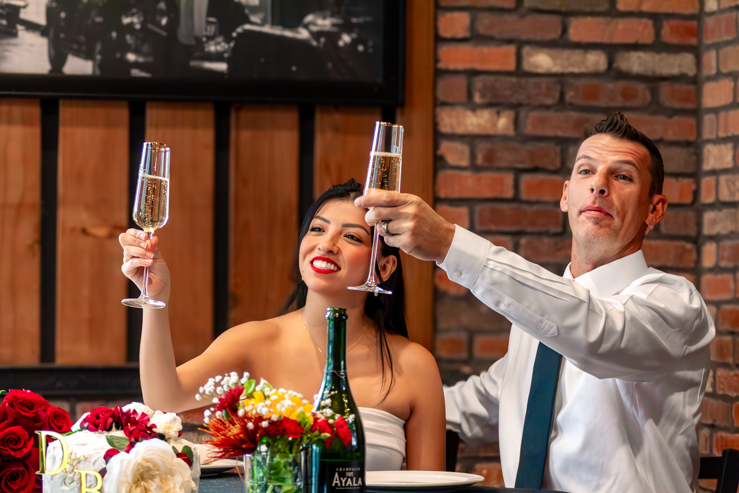 A couple in formal attire toasts with champagne glasses at an elegant table setting.