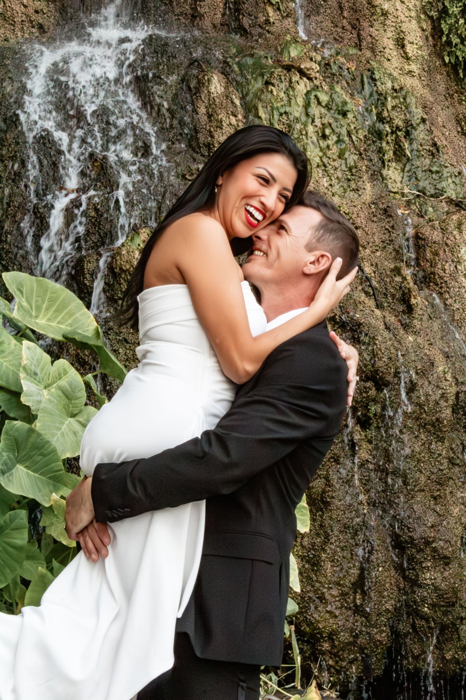 A joyful wedding couple laughing together in front of a cascading waterfall at the Japanese Tea Gardens in San Antonio, Texas.
