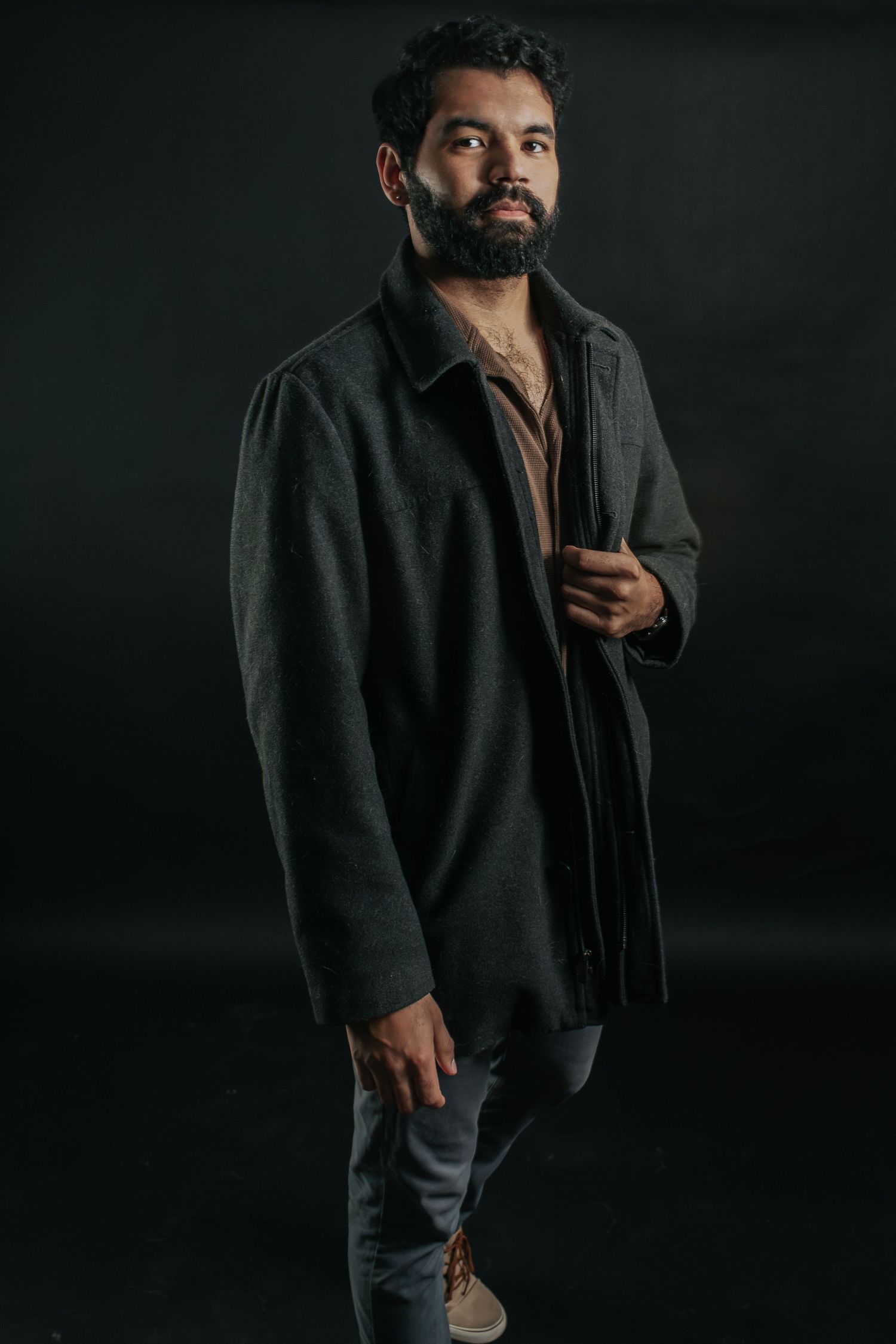 Moody portrait of bearded man in dark coat against black background.
