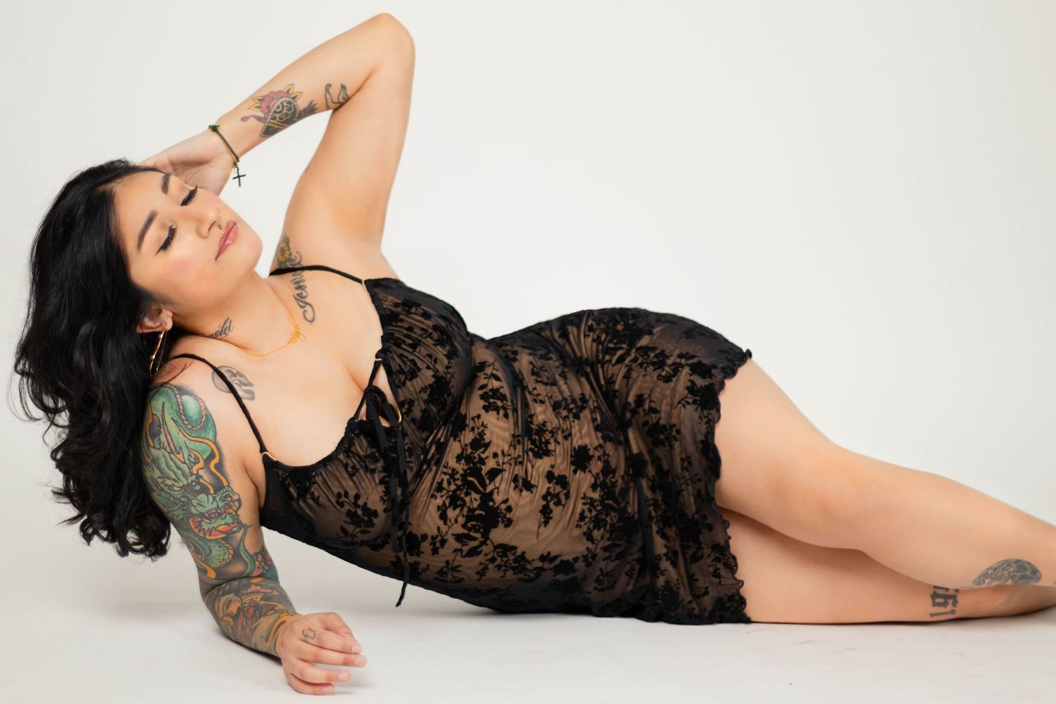 Woman in black lace dress poses on white background with artistic lighting.