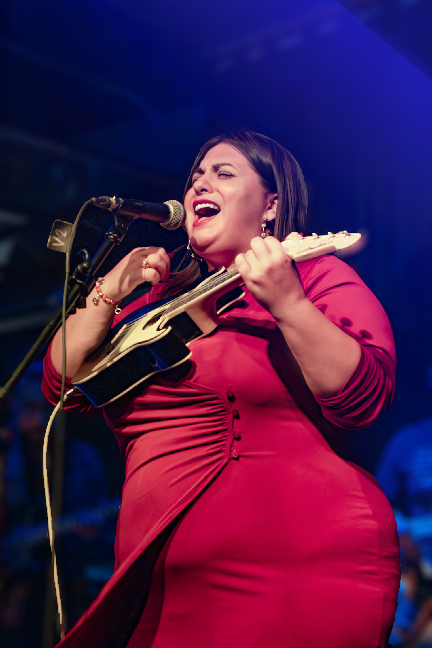 Performer in red dress passionately singing and playing a ukulele on stage with dramatic blue lighting at River North Icehouse in Texas