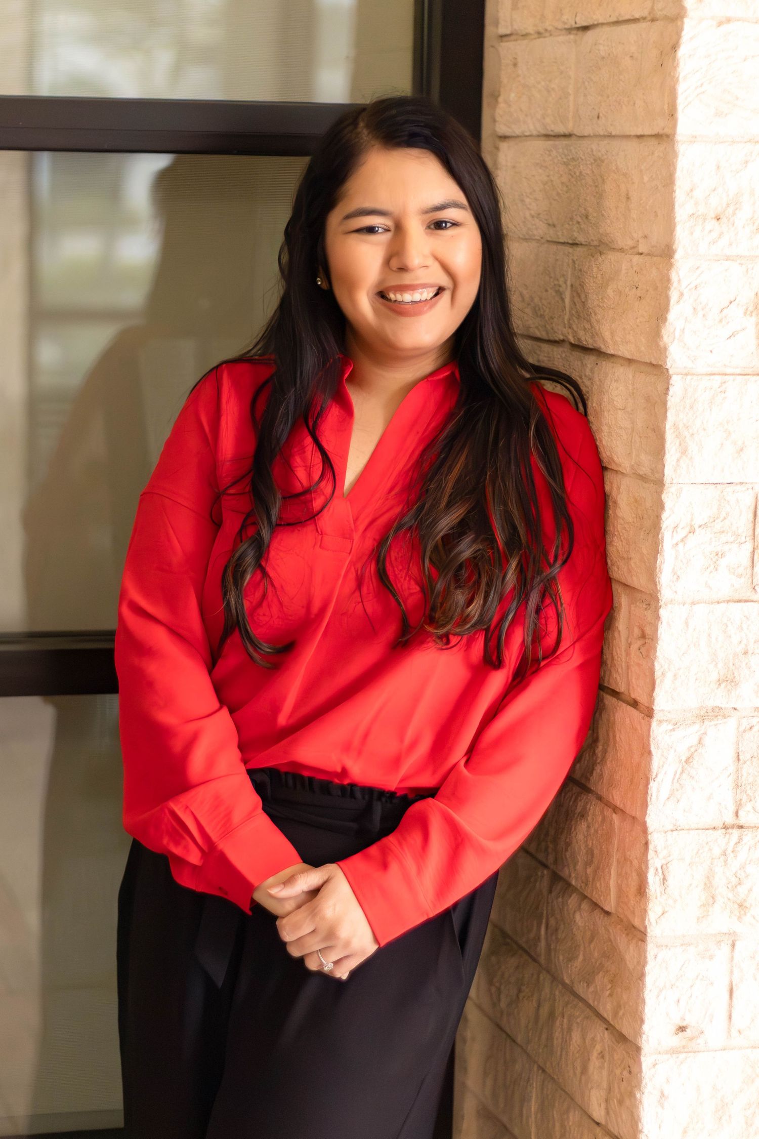 Professional headshot of woman in red blouse smiling against brick wall.