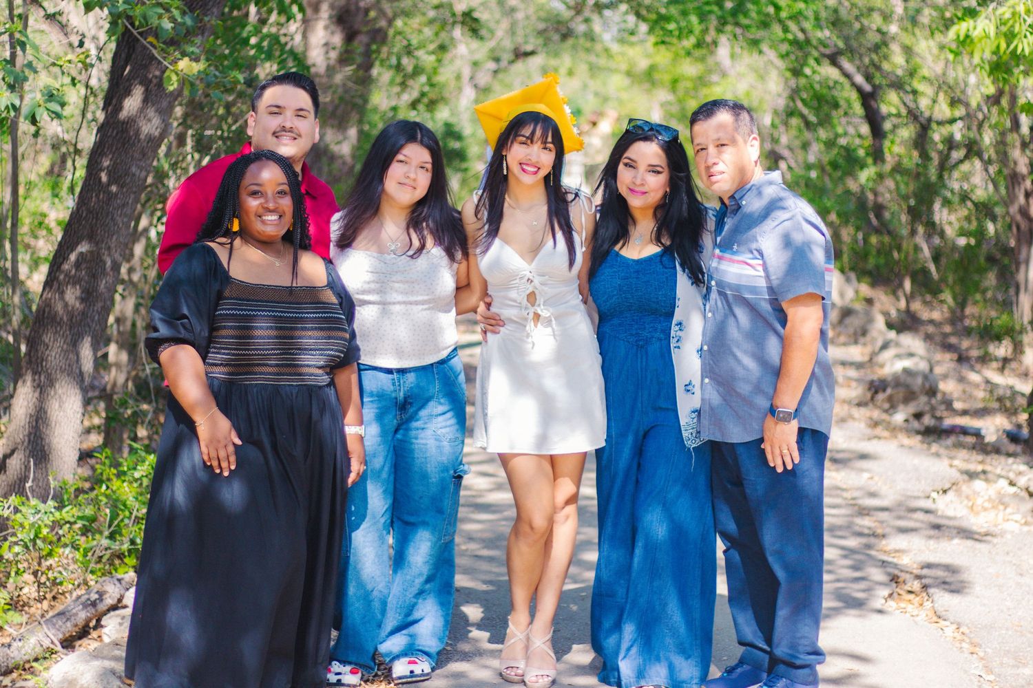 A diverse family stand together smiling on a sunny outdoor trail in casual attire at the Japanese Tea Gardens in San Antonio, Texas