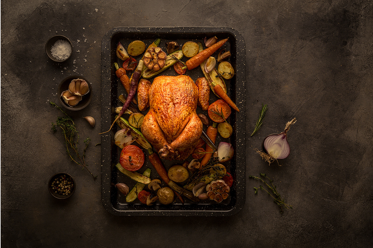 Golden roasted whole turkey with vegetables and herbs in a dark roasting pan.