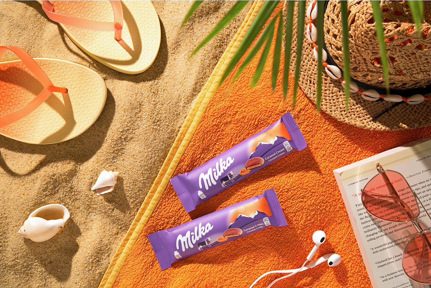 Milka chocolate bars arranged on orange beach towel with summer accessories.