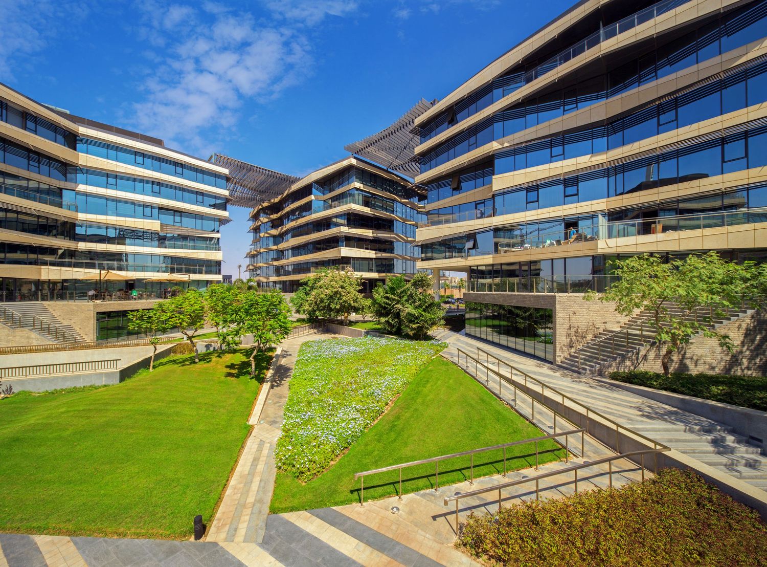 Modern curved office buildings with landscaped gardens under blue sky.