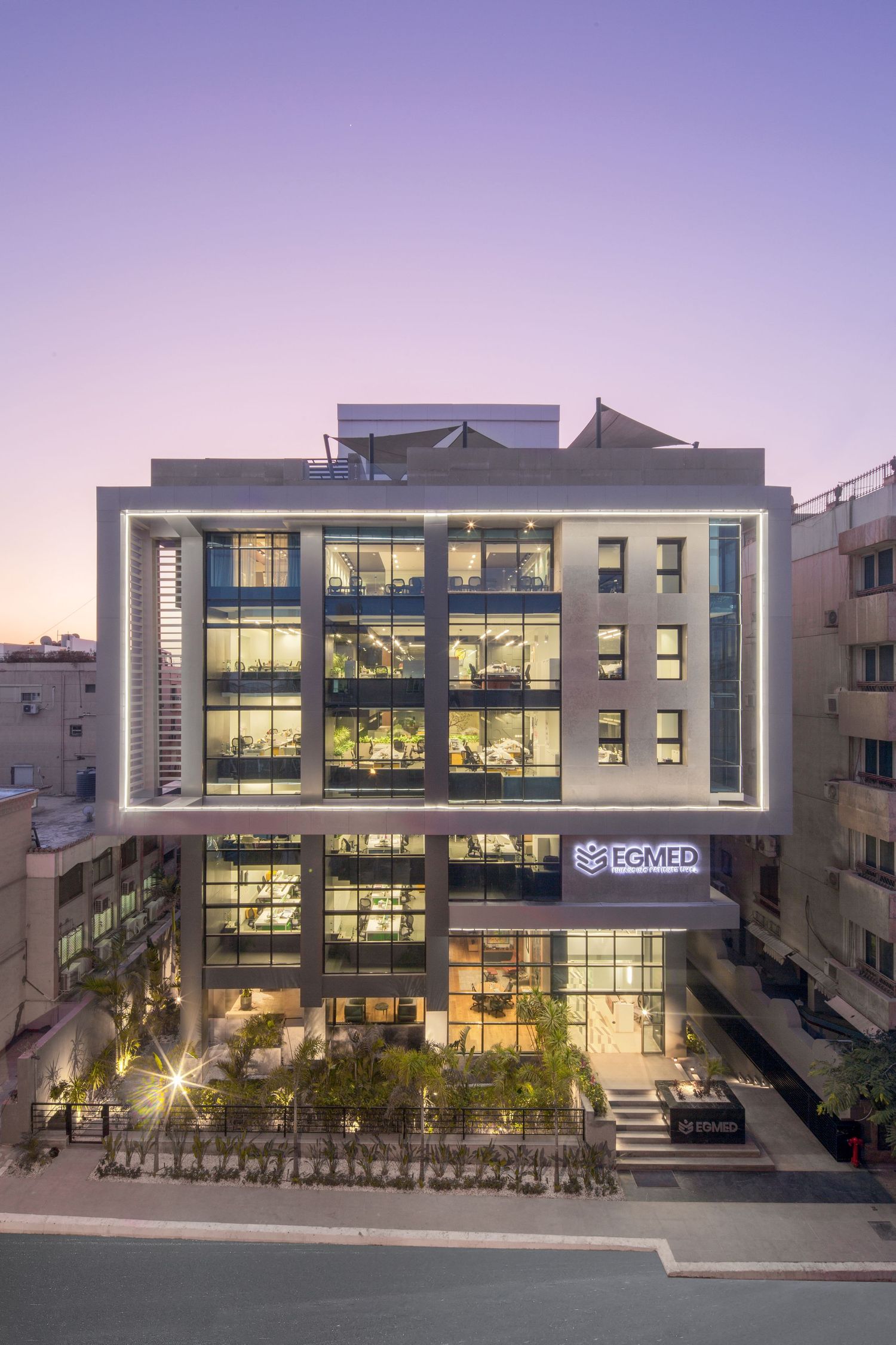 Modern office building illuminated at dusk with glass facade and multiple floors.