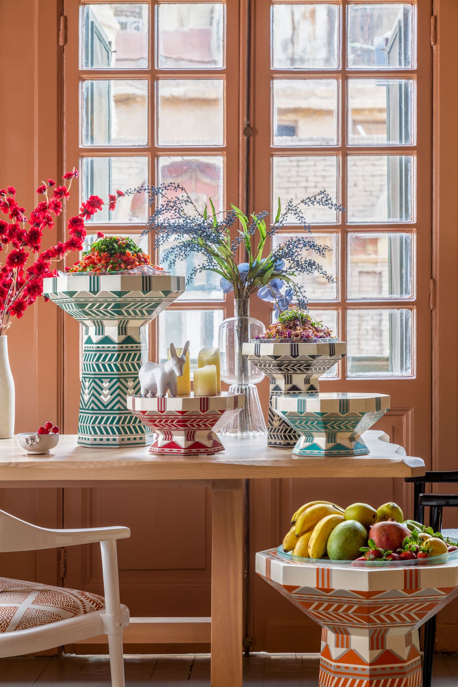 Bright window display with colorful tiered stands holding fruit, flowers and decorative accessories.