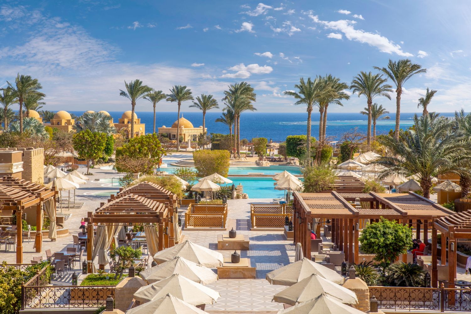 Tropical resort with multiple pools, palm trees and beach cabanas overlooking the ocean.