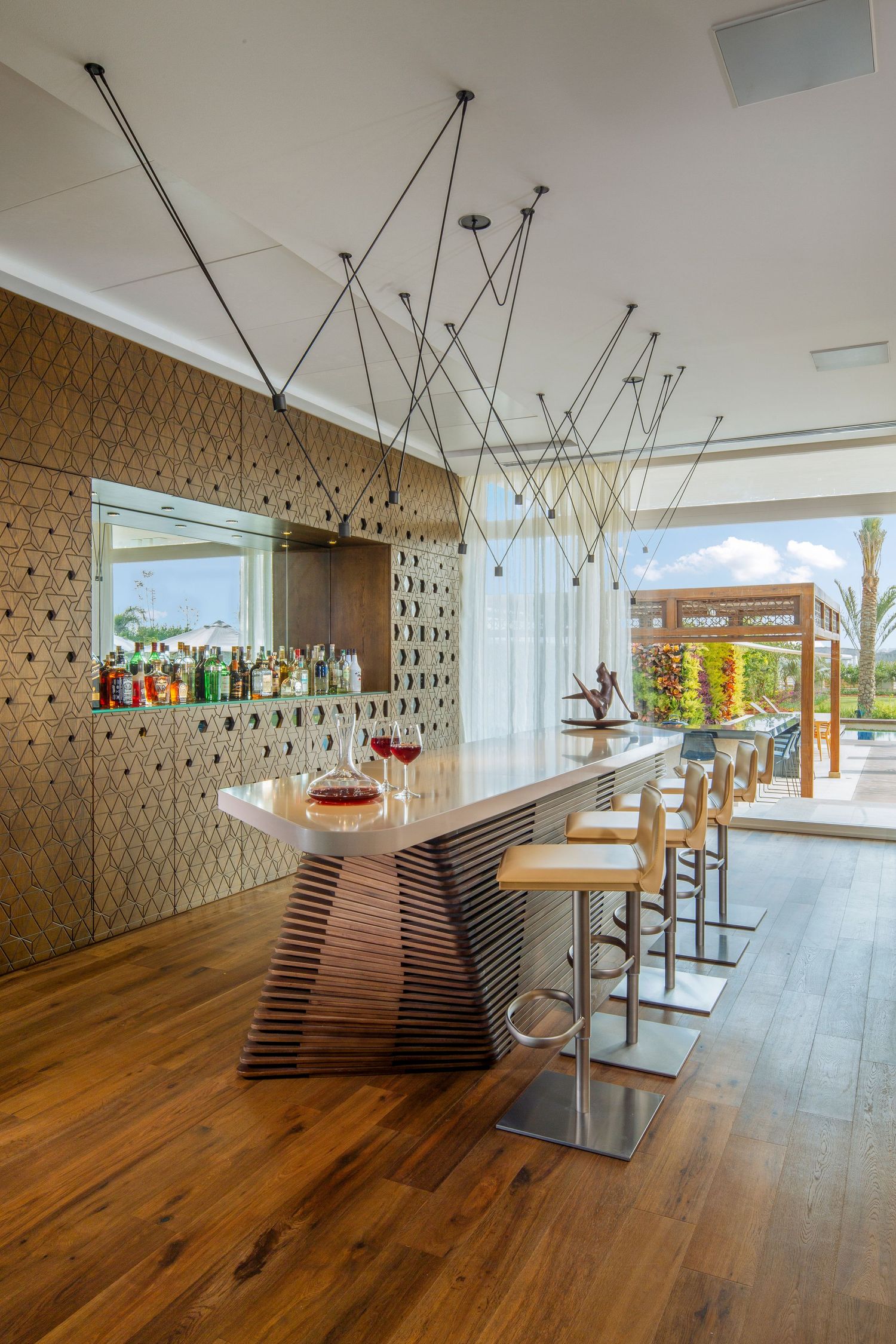 Luxurious home bar with geometric wall panels, wooden floors, and modern suspended lighting fixtures.