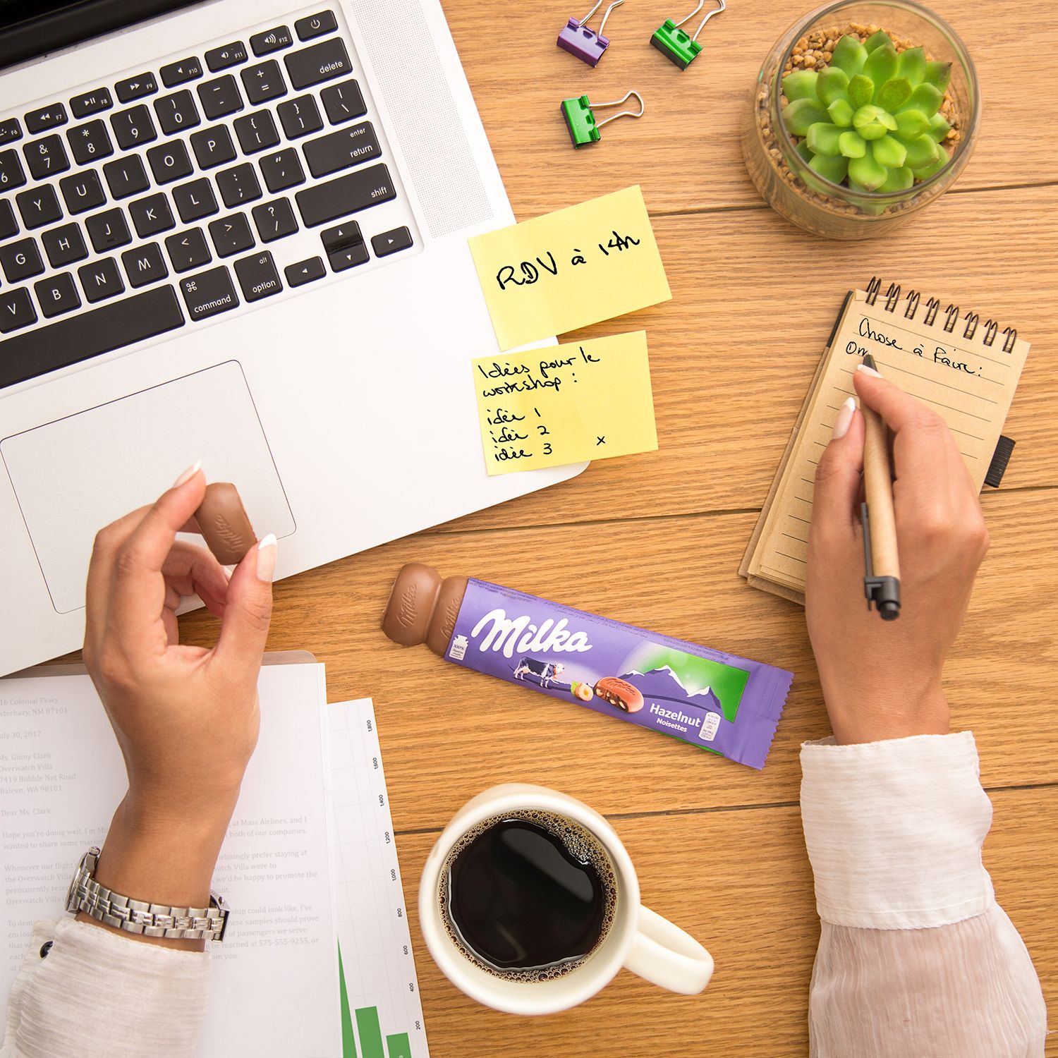 Workspace with laptop, sticky notes, coffee, and Milka chocolate bar showing modern office essentials.