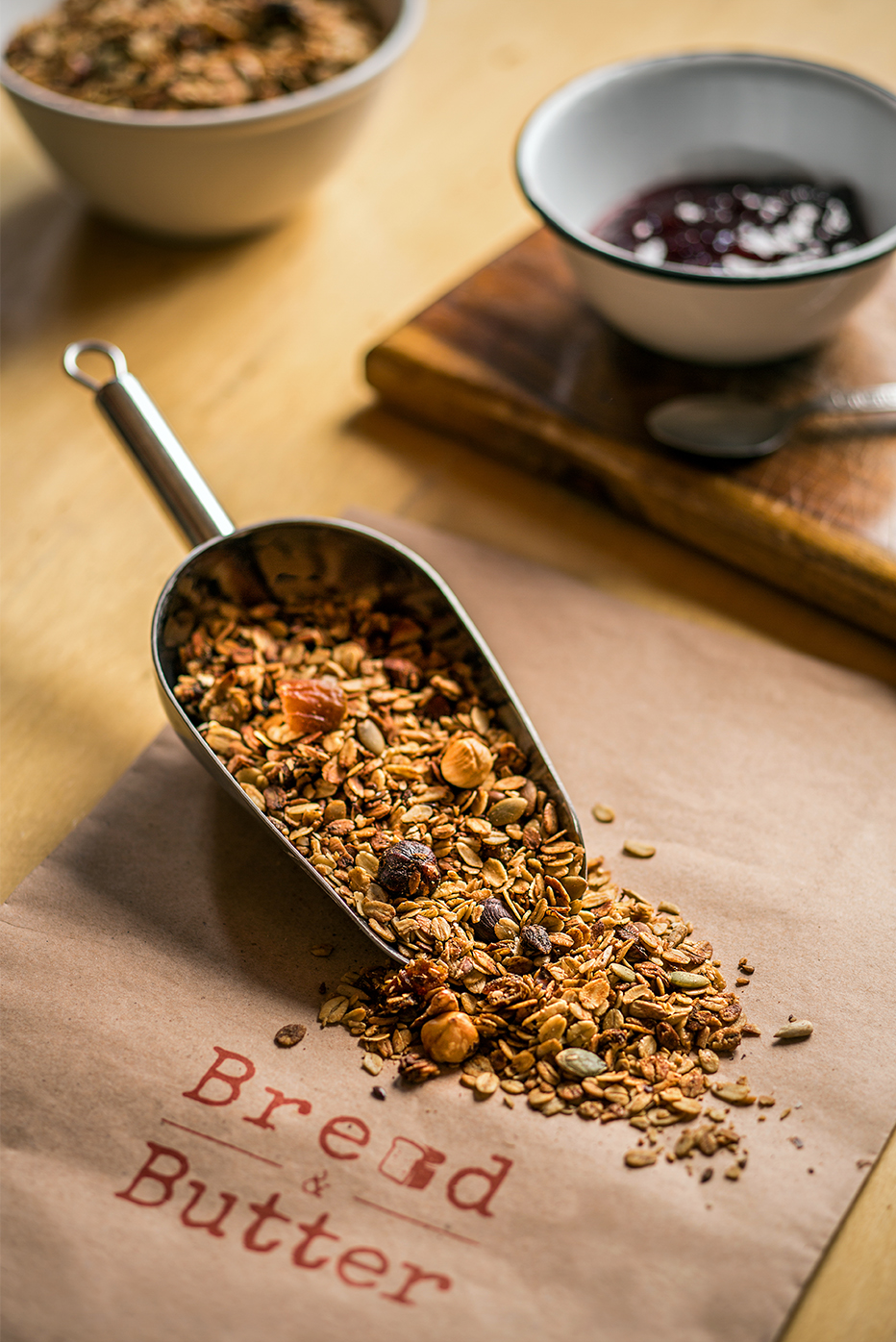 Artisanal granola mixture spilling from a metal scoop onto branded packaging.
