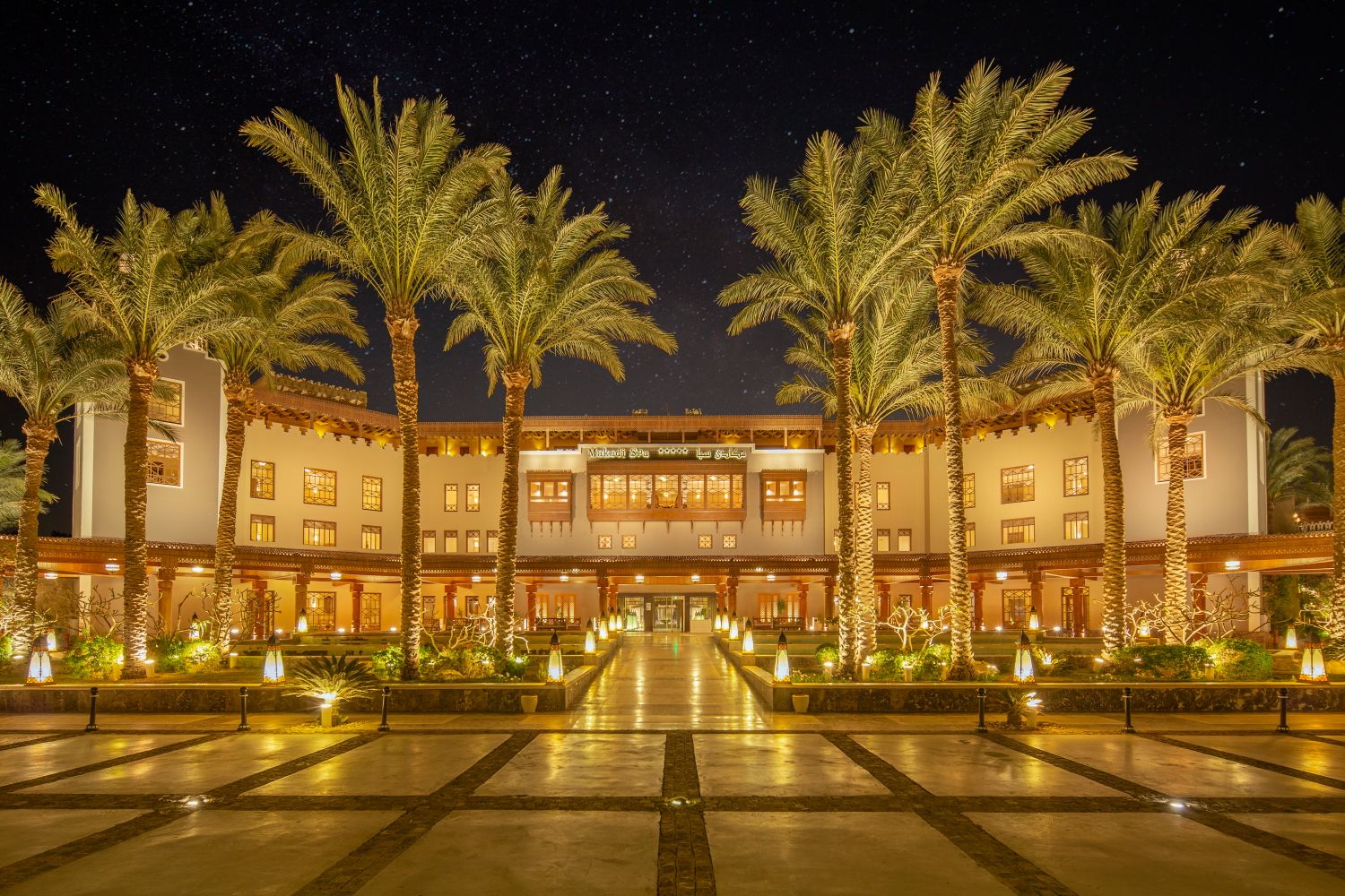 Luxurious hotel exterior illuminated at night with palm trees and reflection pool.