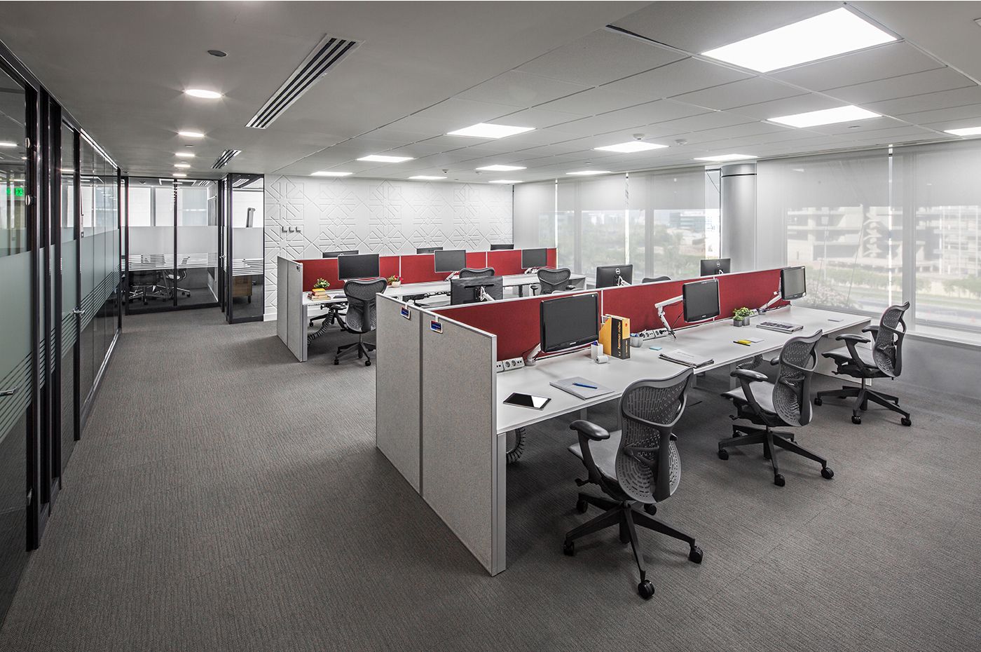 Spacious office area with red and white workstations, ergonomic chairs, and bright fluorescent lighting.