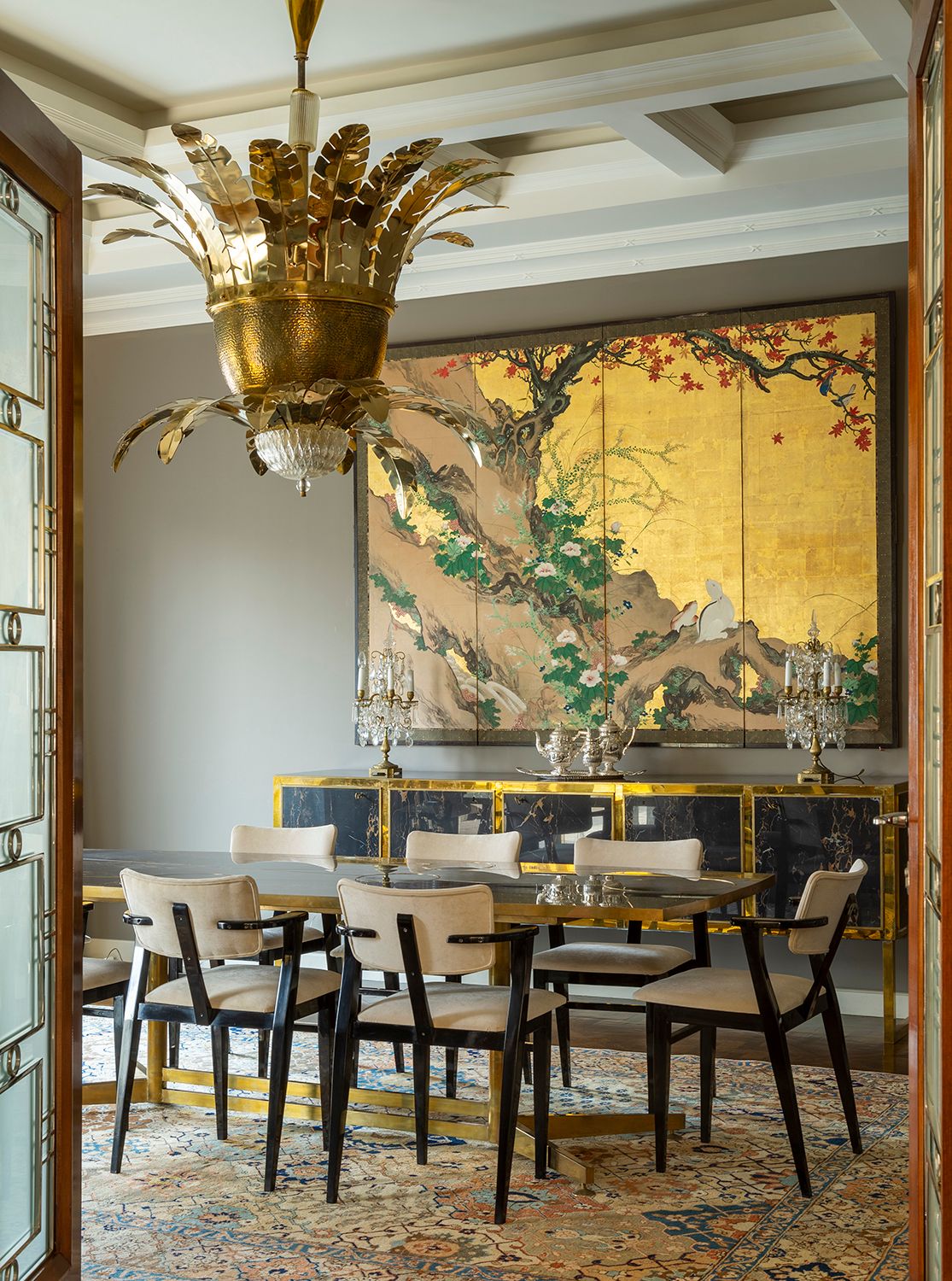 Elegant dining area with large gold palm chandelier and Asian-inspired wall art on gold background.
