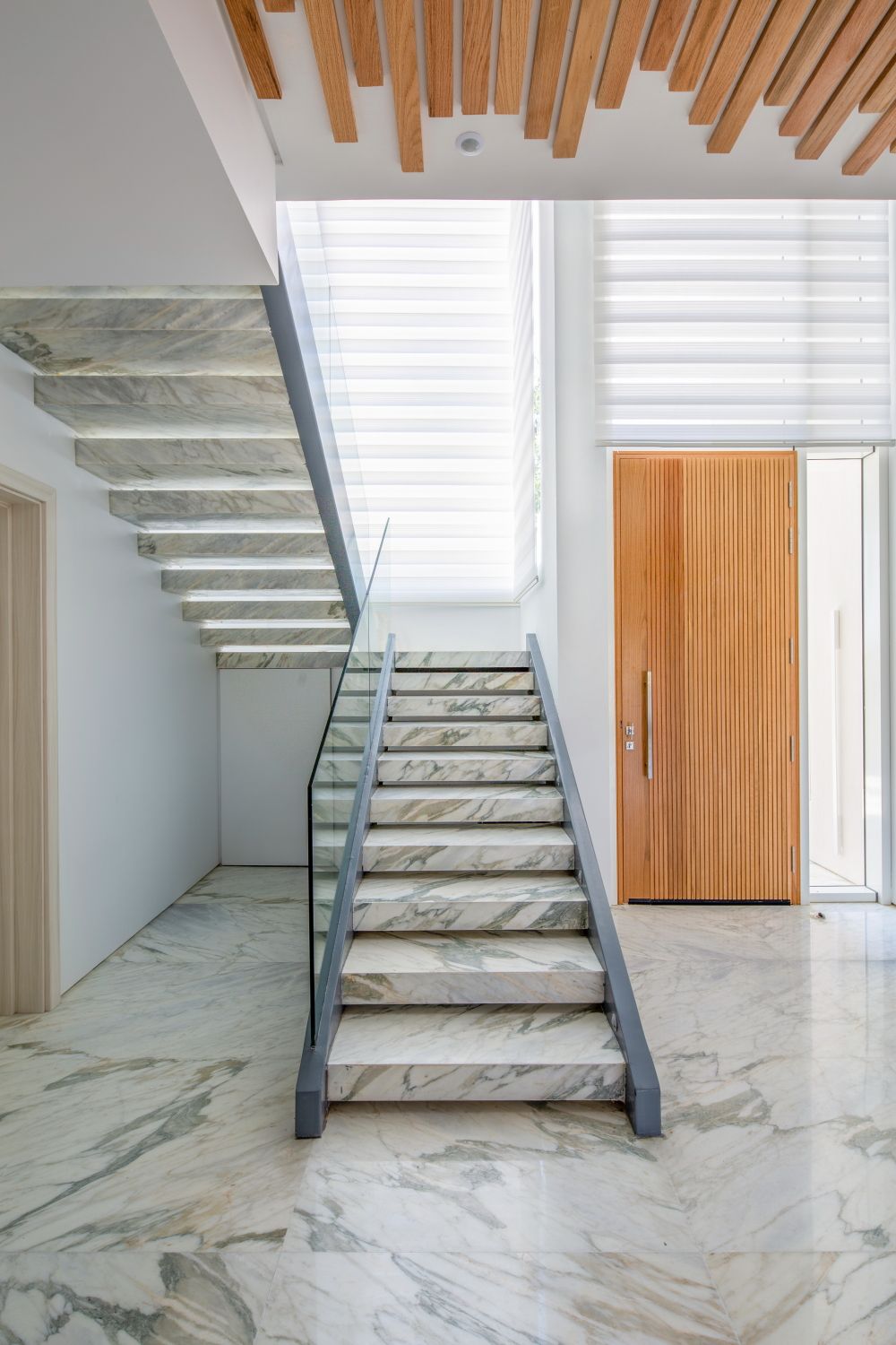 Elegant marble staircase with wooden ceiling details and glass railing.