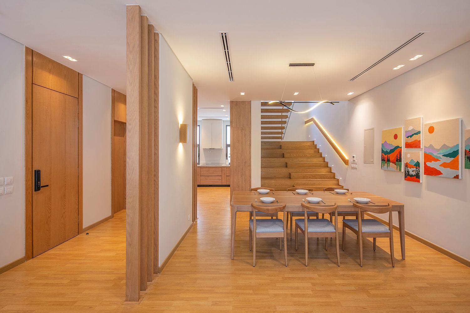 Contemporary dining area with wooden stairs, neutral tones, and colorful wall art.