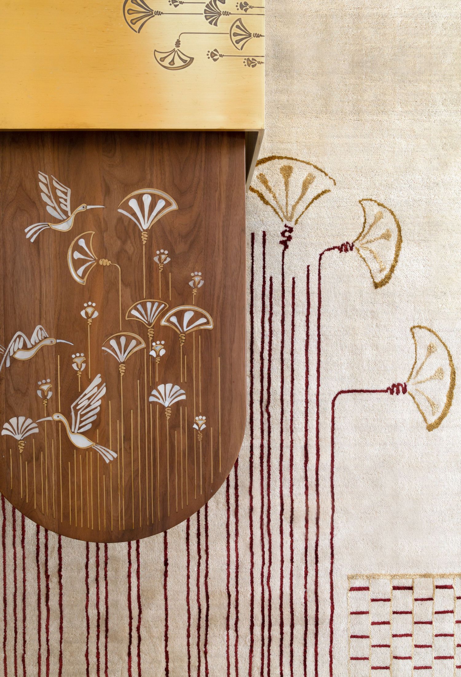 top shot of an elegant coffee table with a carpet featuring bird and fan motifs in gold and burgundy on wood and fabric surfaces.