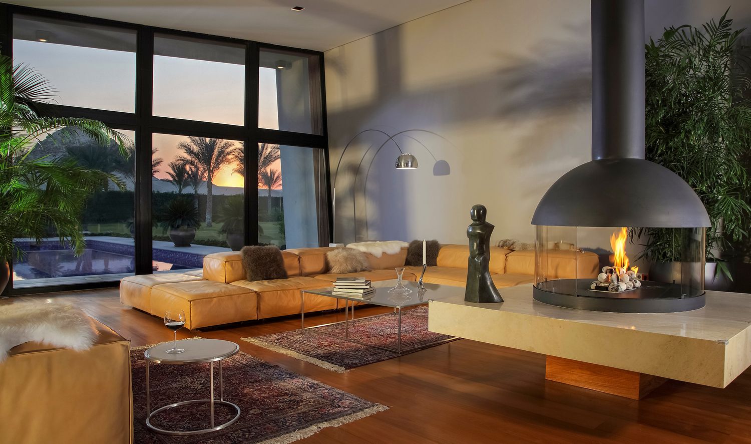 Contemporary living room with suspended fireplace and large windows showcasing sunset view.