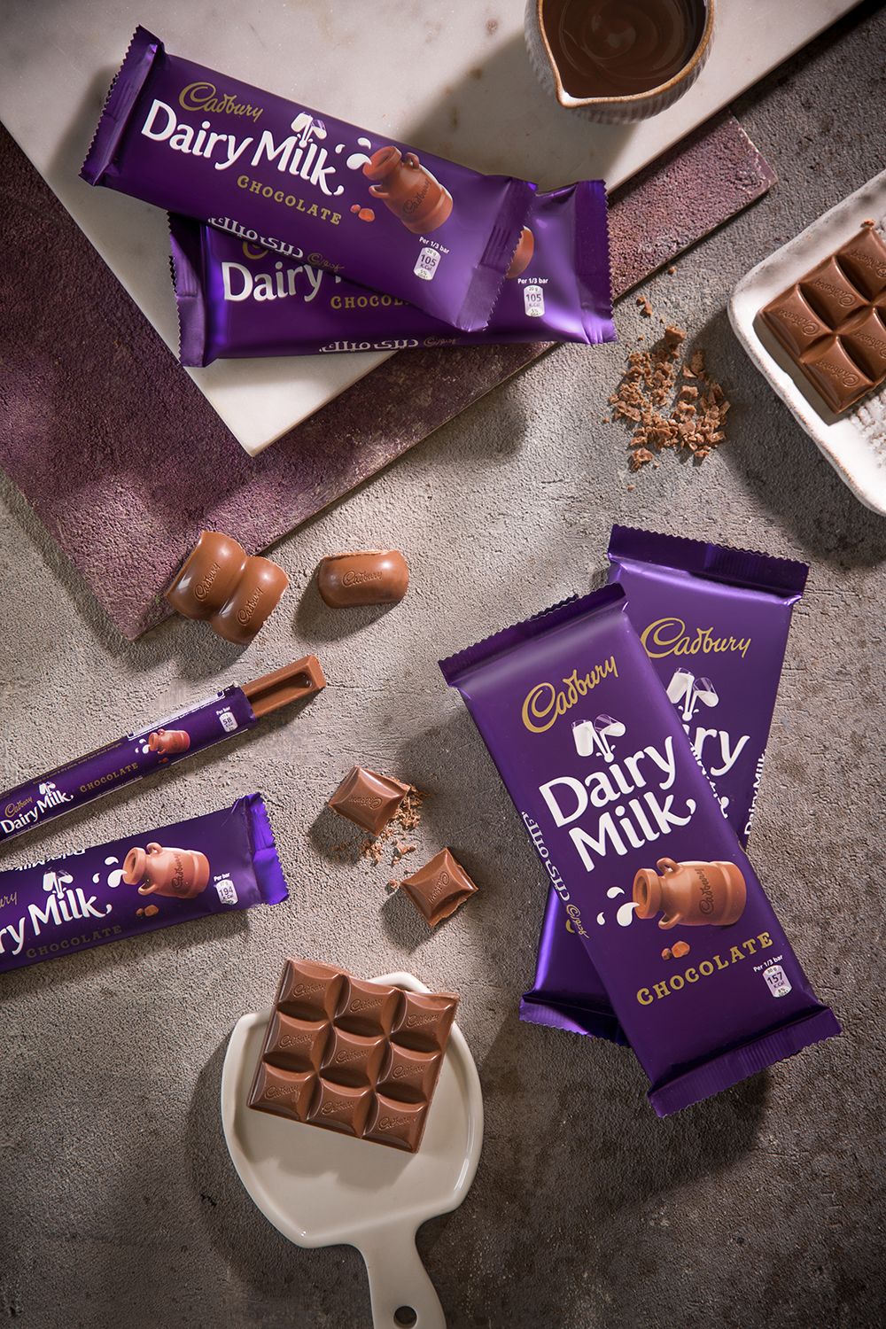 Overhead view of scattered Cadbury Dairy Milk chocolate bars and pieces on dark surface.