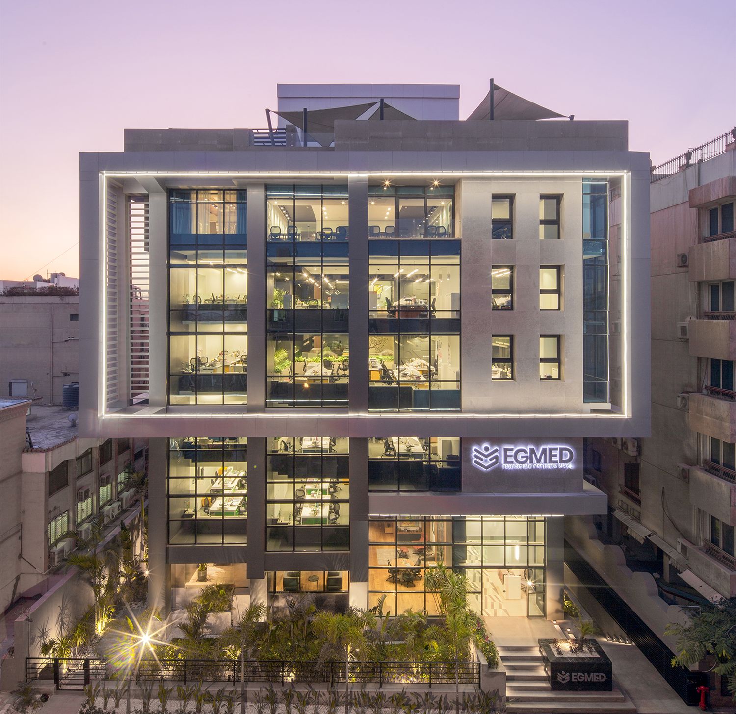 Modern office building illuminated at dusk with glass facade and geometric design.