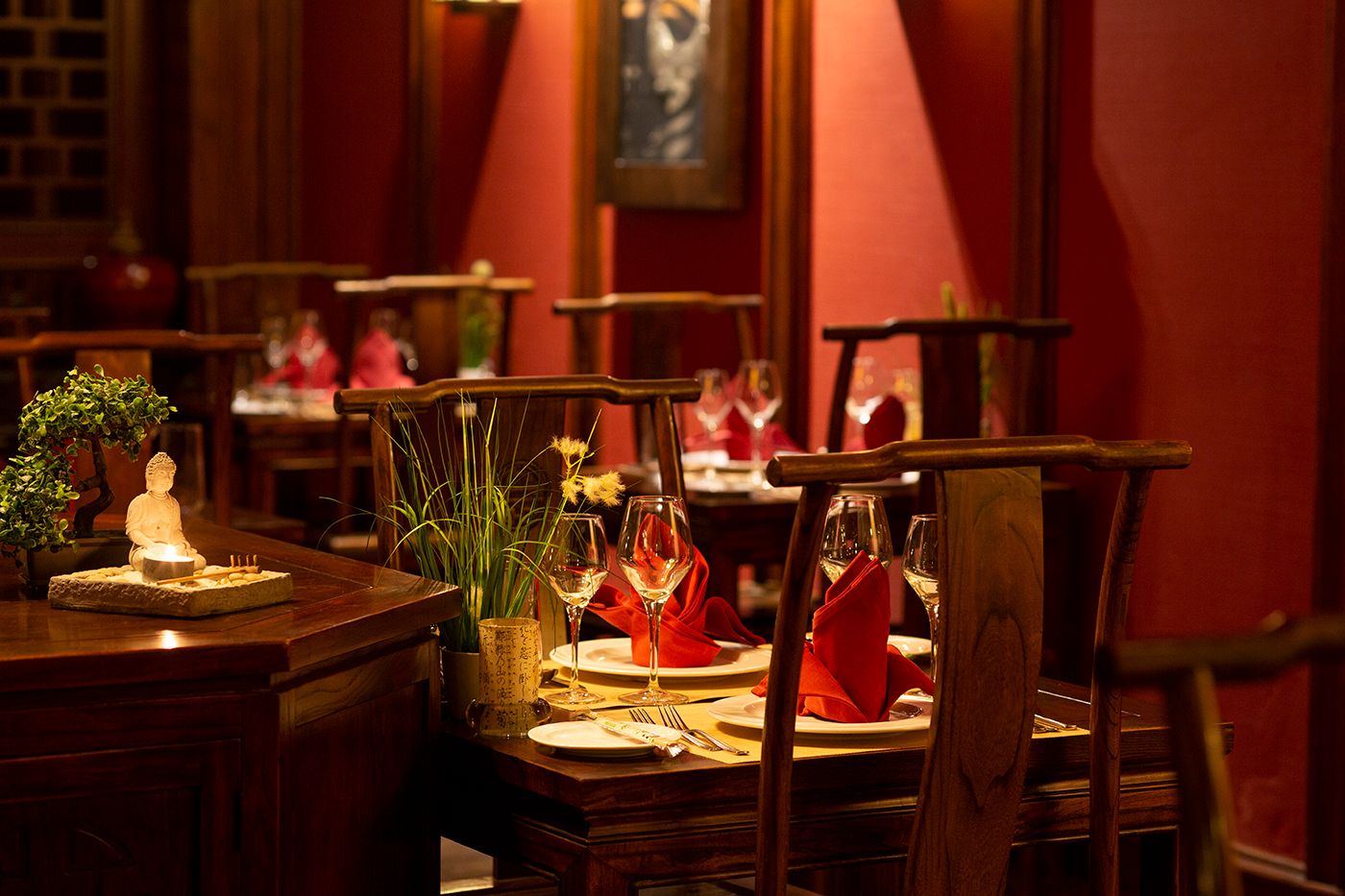 Intimate restaurant interior with red walls and elegant table settings in warm lighting.