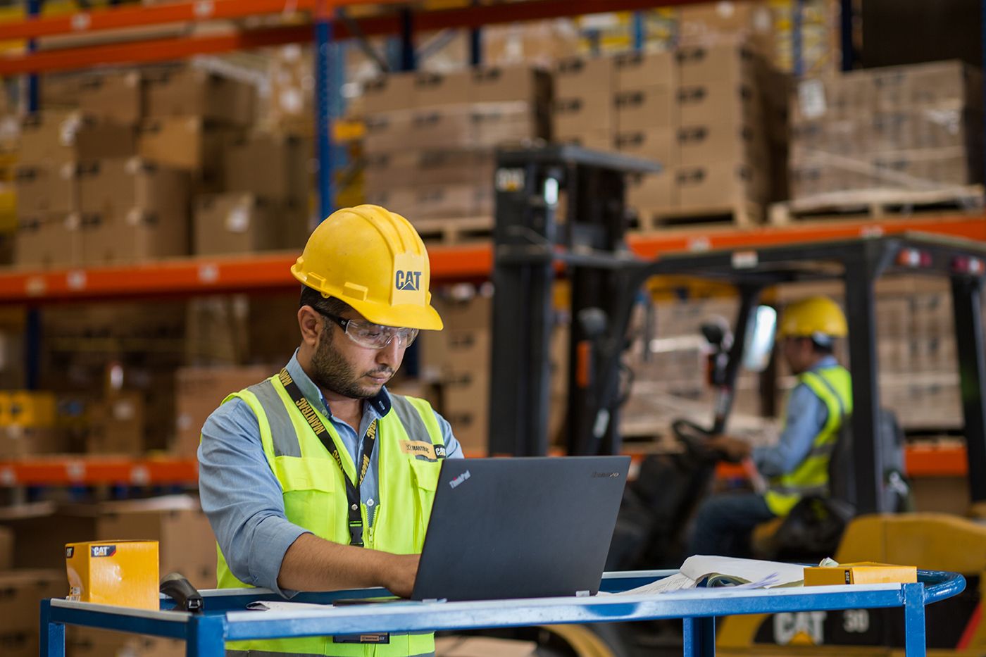 Warehouse worker in safety vest using laptop at mobile workstation.