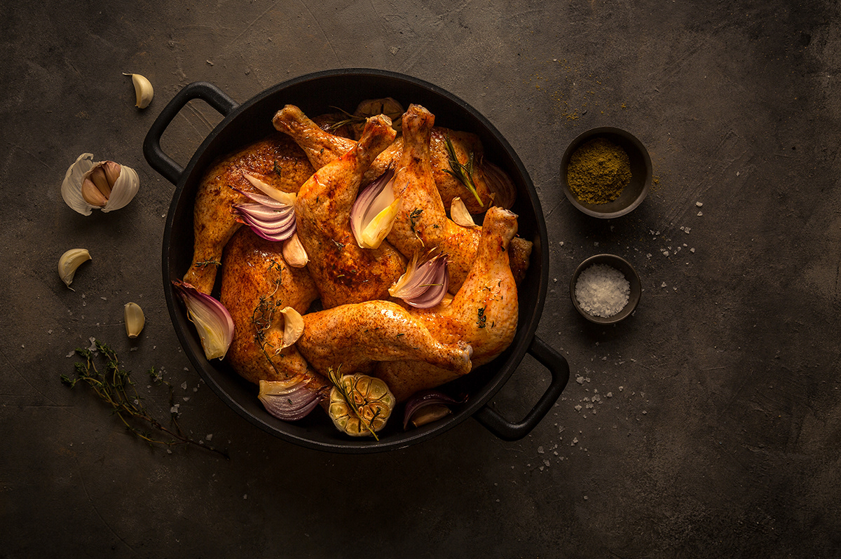 Roasted chicken pieces with vegetables and seasonings in a cast iron skillet.