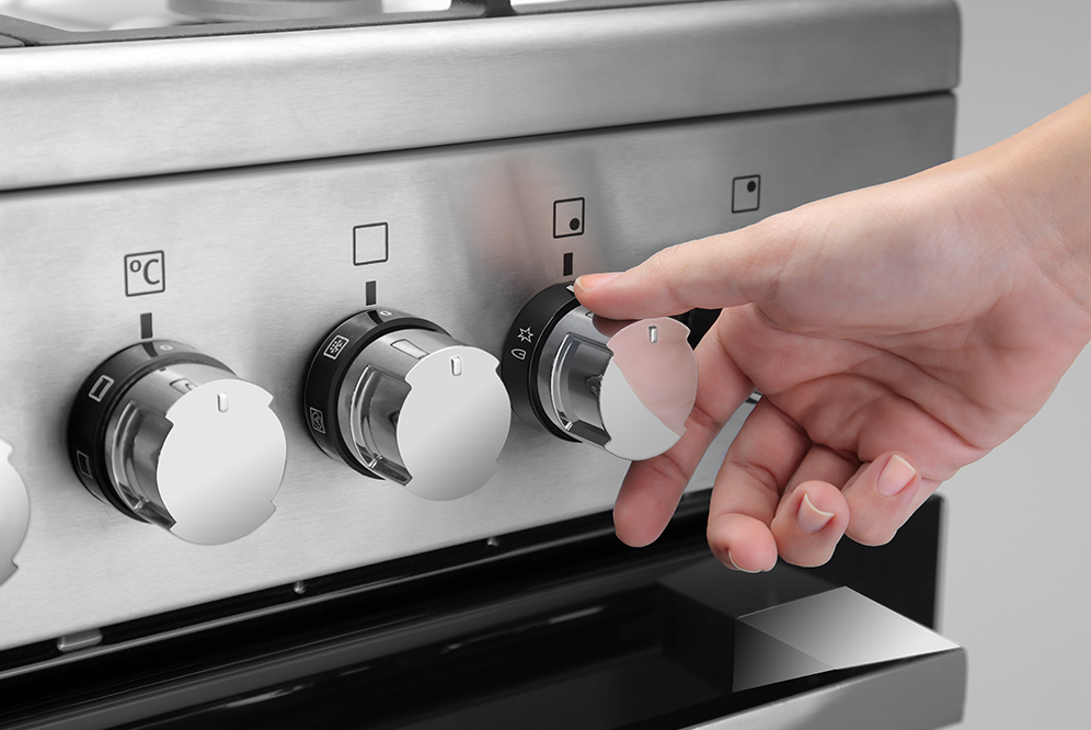 Close-up of hand adjusting temperature control knobs on stainless steel stove.