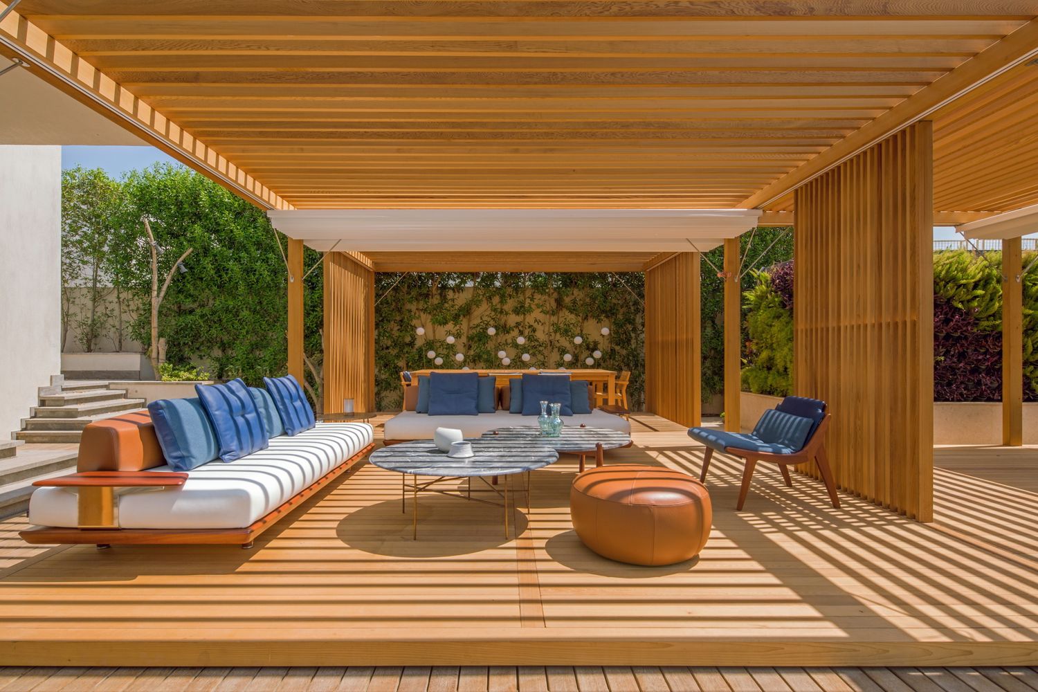 Luxurious wooden deck lounge area with blue cushioned seating and leather poufs under timber beams.