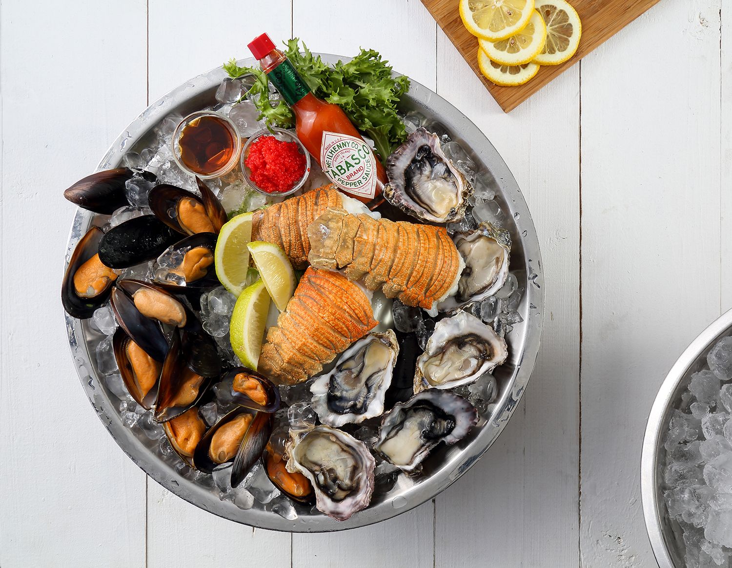 Fresh seafood platter with lobster tail, oysters, and mussels on ice with lemon and sauce.